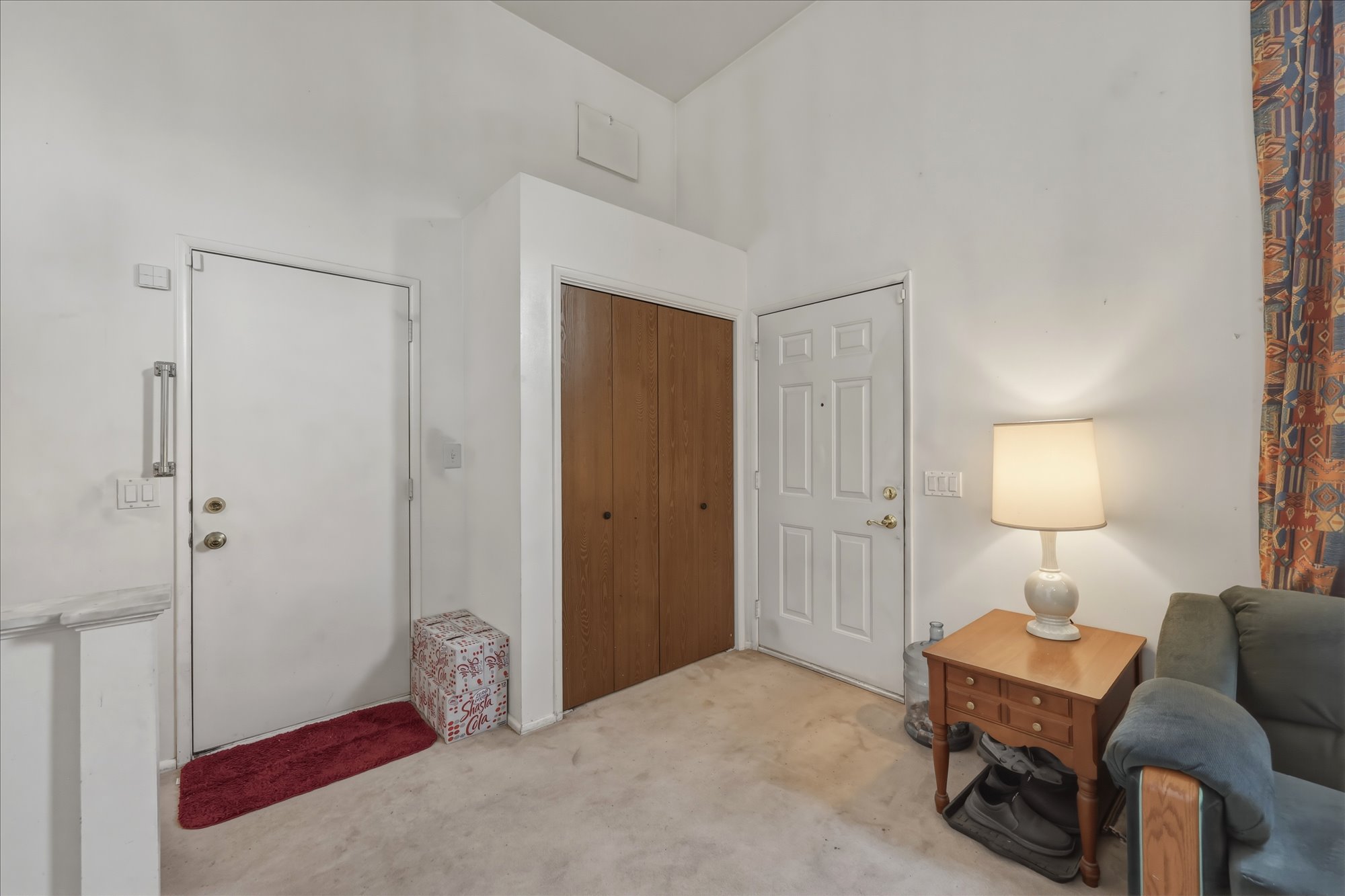 Entryway featuring two white doors, wood-finish closet doors, and carpet flooring