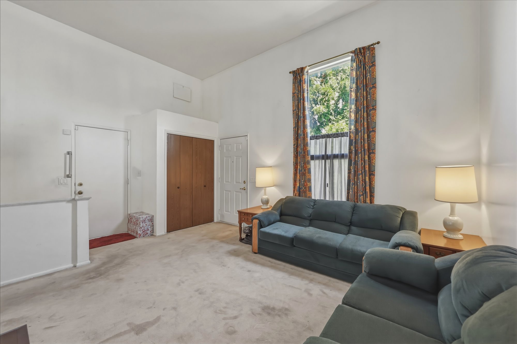 Spacious living area featuring a high ceiling, neutral carpet flooring, and a window providing natural light
