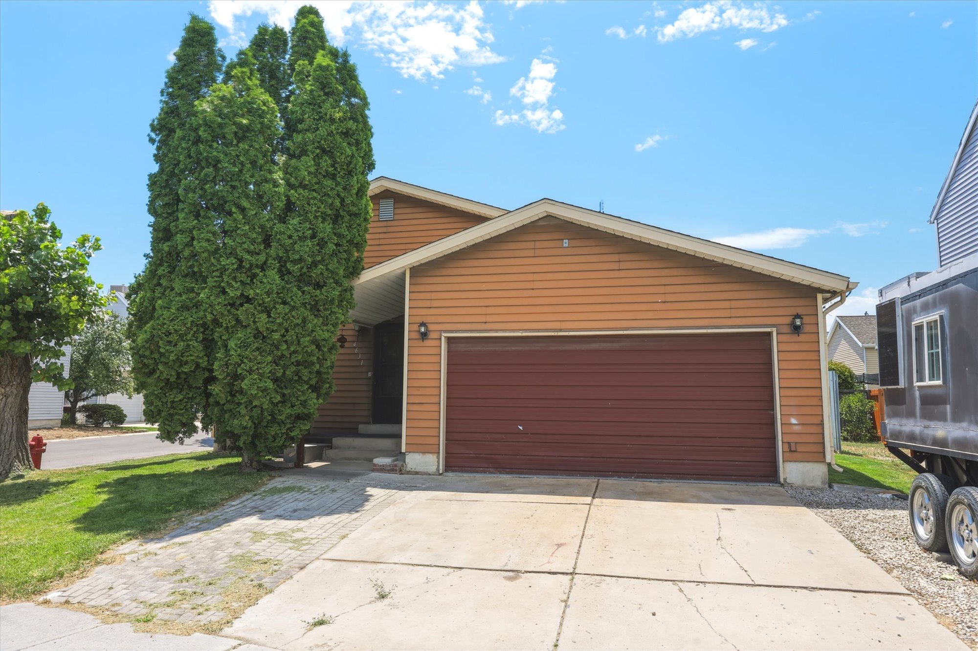 Split-level home featuring horizontal siding, a two-car garage with a brown door, and a concrete driveway