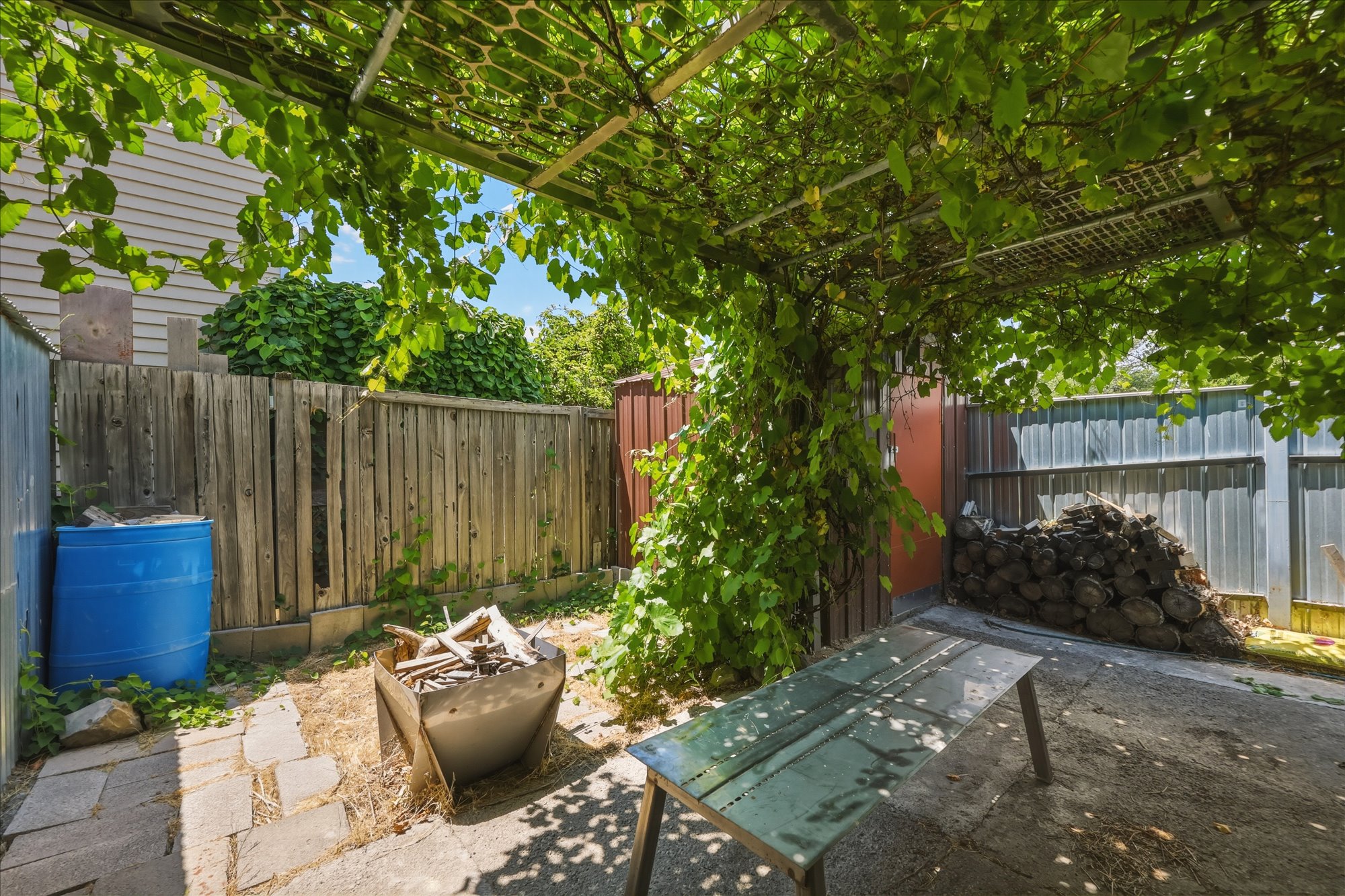 Outdoor patio area featuring a metal pergola with mature vine coverage, providing natural shade