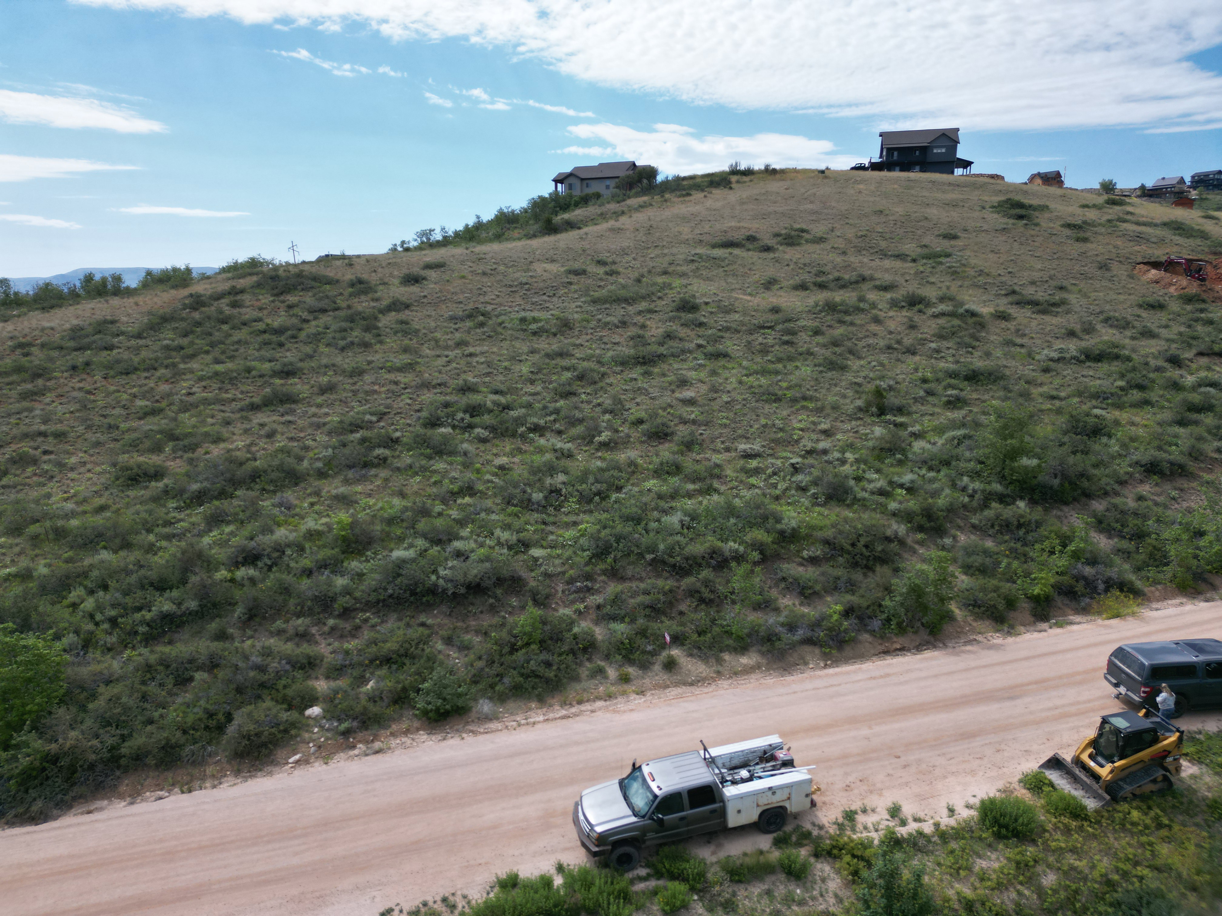 Expansive hillside lot featuring natural shrubbery and a dirt road frontage