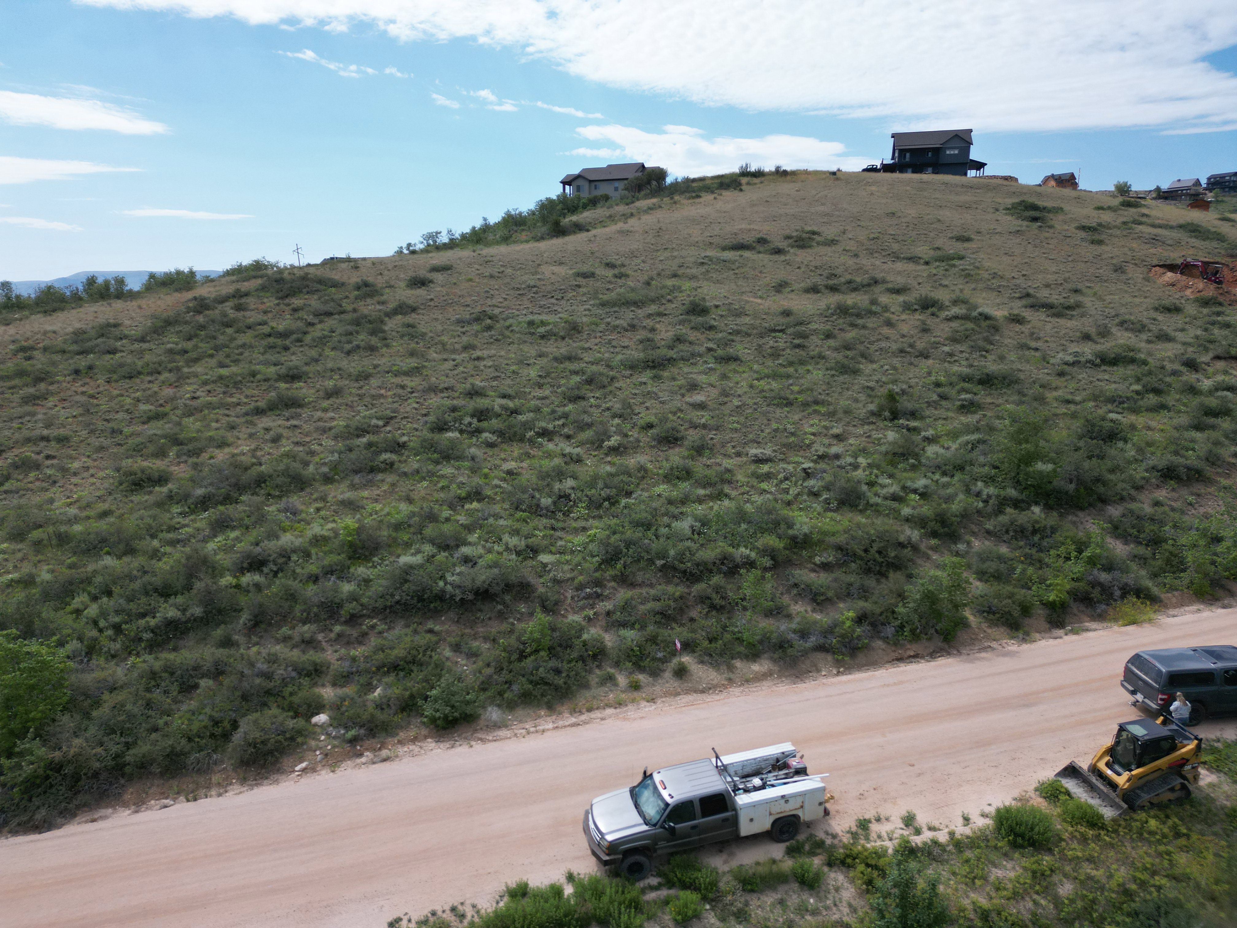 Expansive hillside property featuring natural vegetation, a clear blue sky, and distant structures