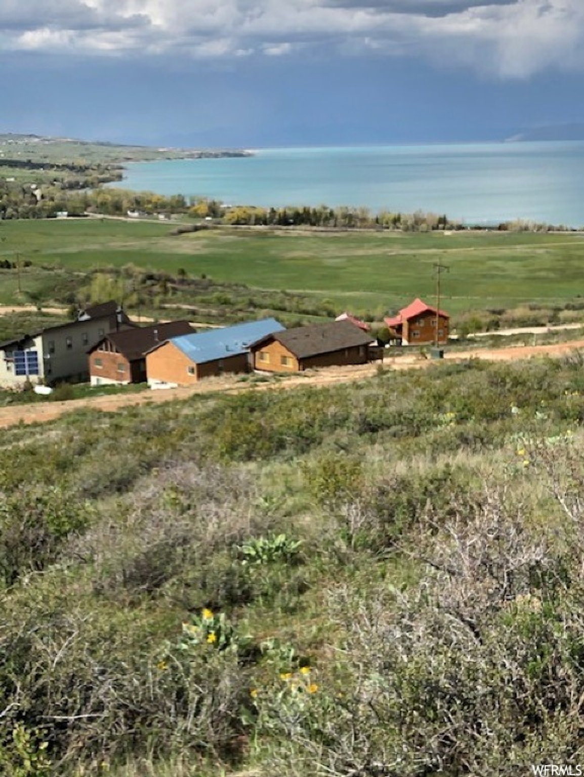 Expansive landscape featuring distant water, open fields, and residential structures