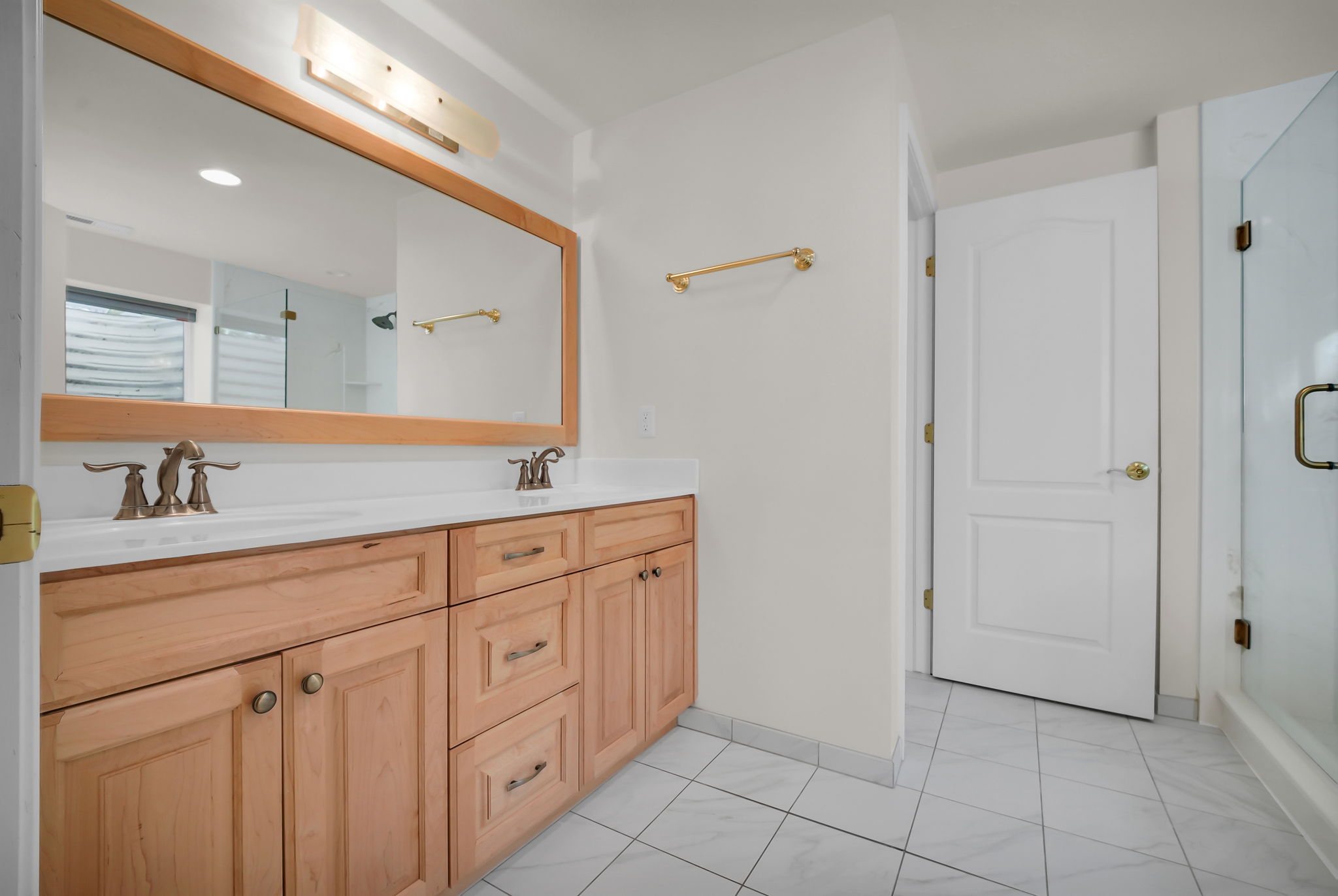 Bathroom featuring a double vanity with light wood cabinetry, white countertops, and dual basin sinks with bronze-finish fixtures