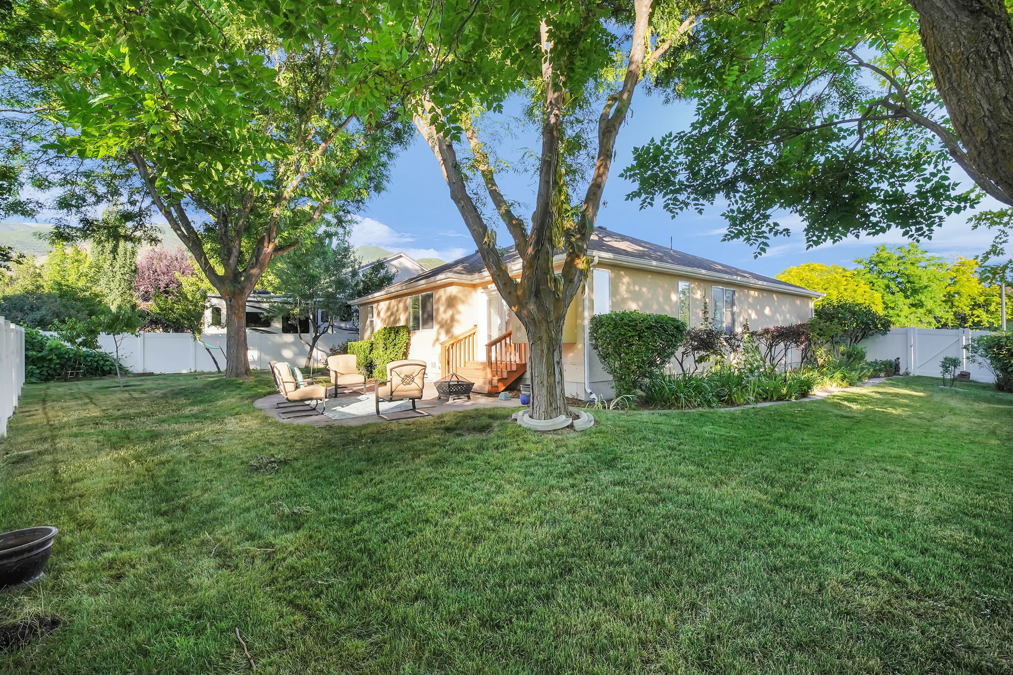 Expansive backyard featuring a lush lawn, mature shade trees, a stone patio, and a privacy fence