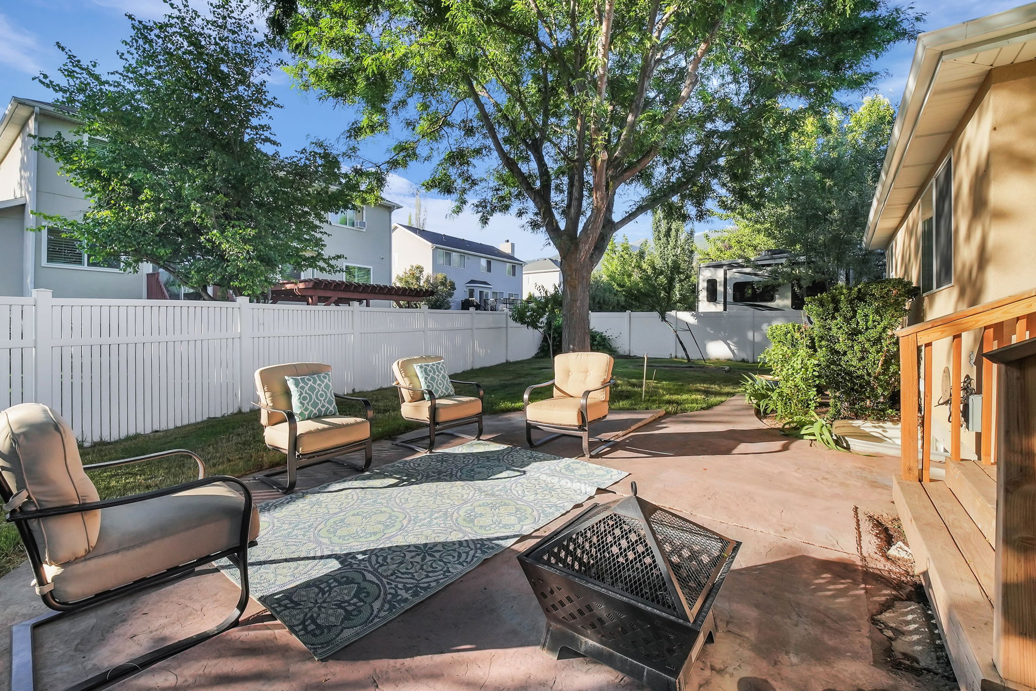 Expansive backyard featuring a concrete patio, mature trees, and a white privacy fence