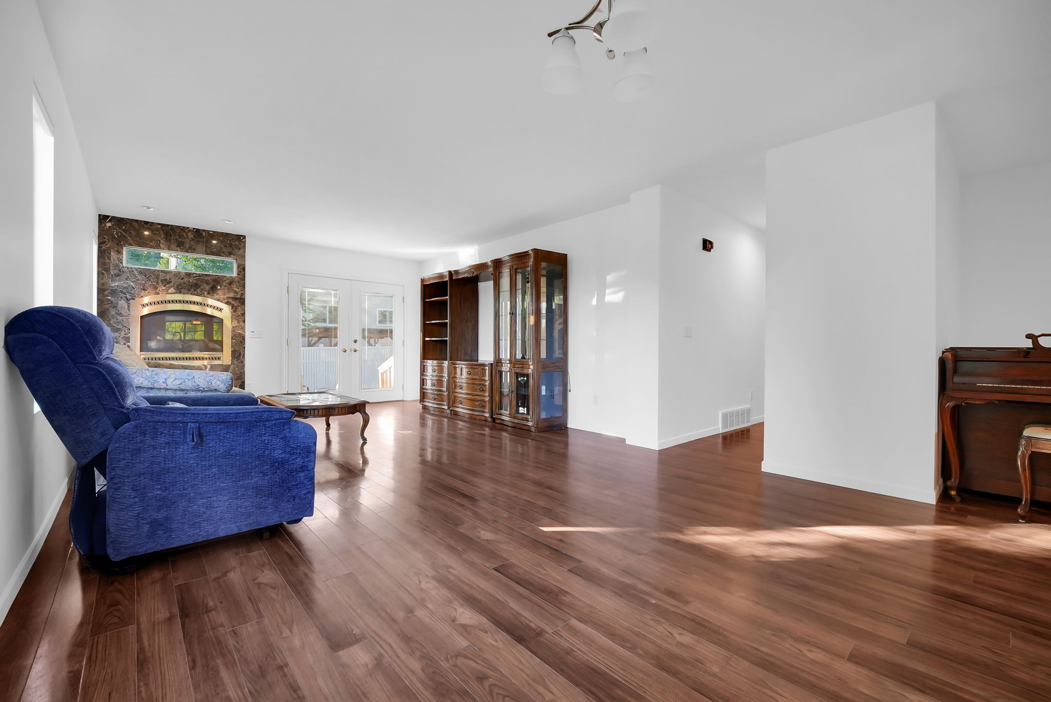 Spacious living area featuring wood-finish flooring, a fireplace with a stone surround, and French doors