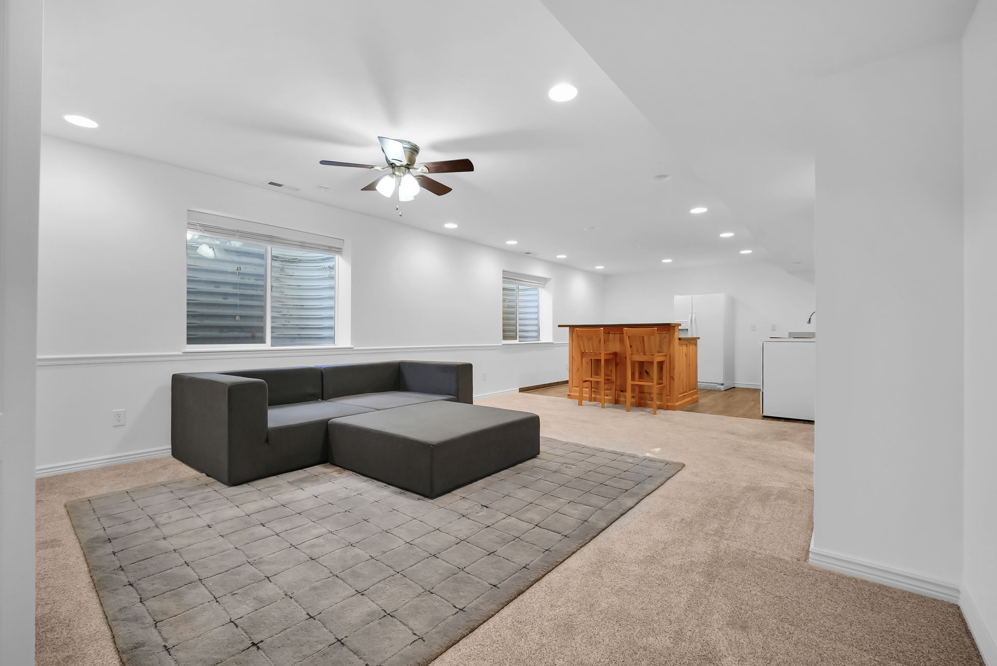 Spacious lower-level area with recessed lighting, ceiling fan, carpet flooring, and two egress windows