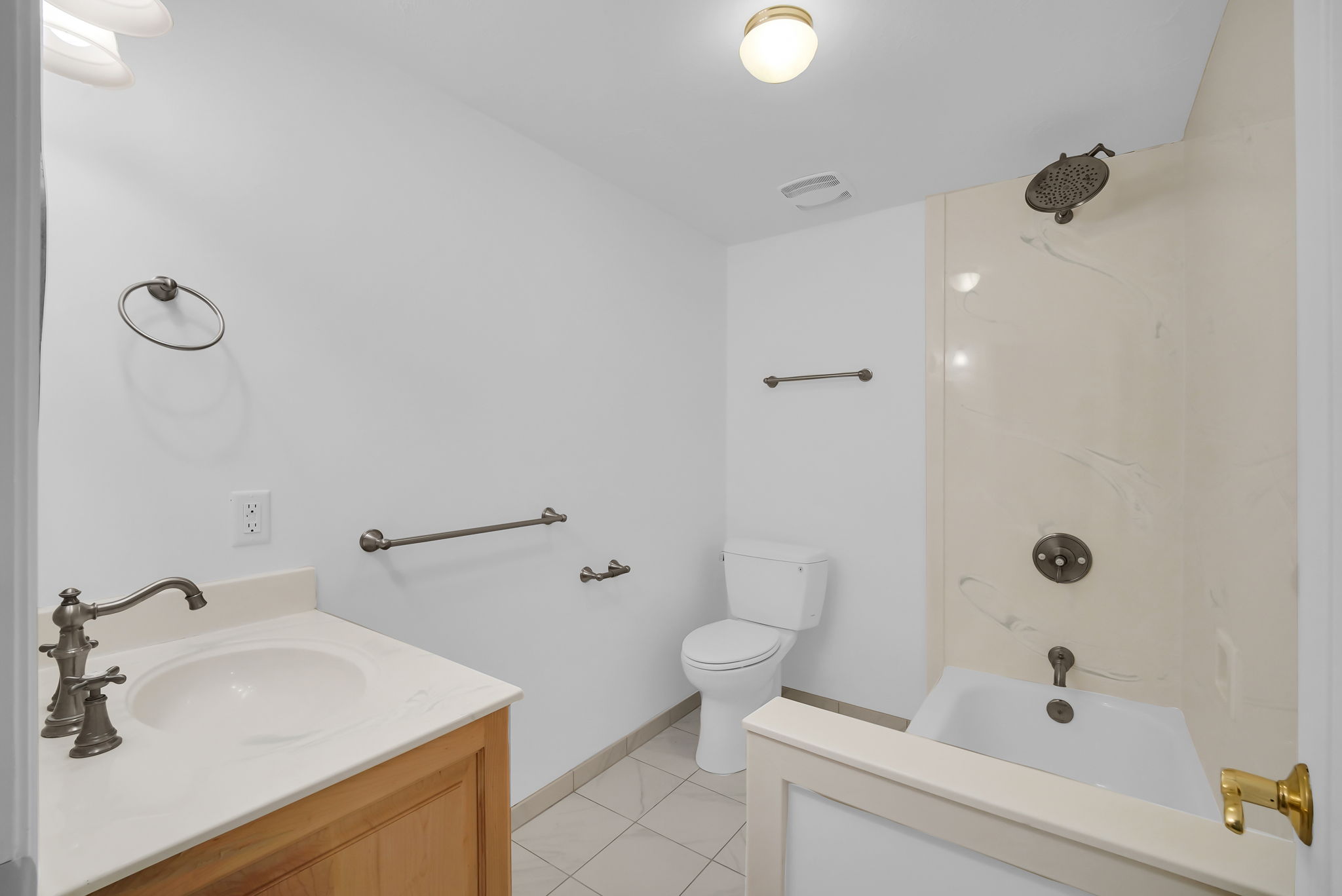 Bathroom featuring a wood vanity with a single basin sink and bronze-finish faucet, a toilet, a shower-over-tub combination with a wall-mounted showerhead, and a tiled floor