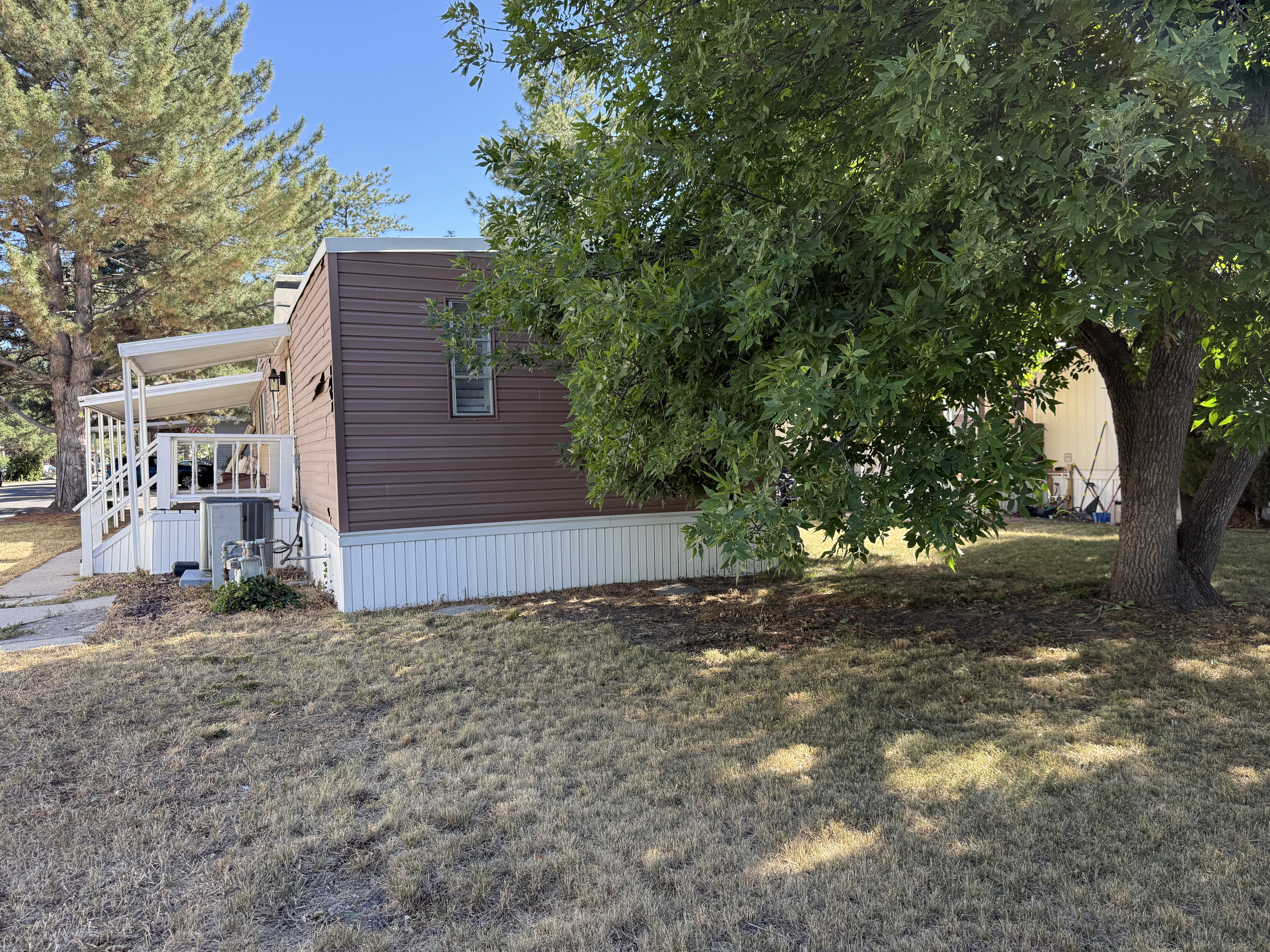 Brown siding exterior with white skirting, featuring a covered porch with white railings