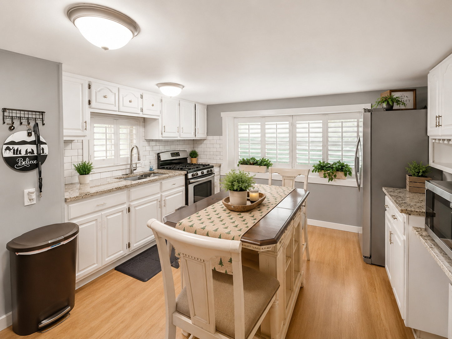 Well-appointed kitchen featuring white cabinetry, granite countertops, subway tile backsplash, stainless steel appliances, and wood-finish flooring