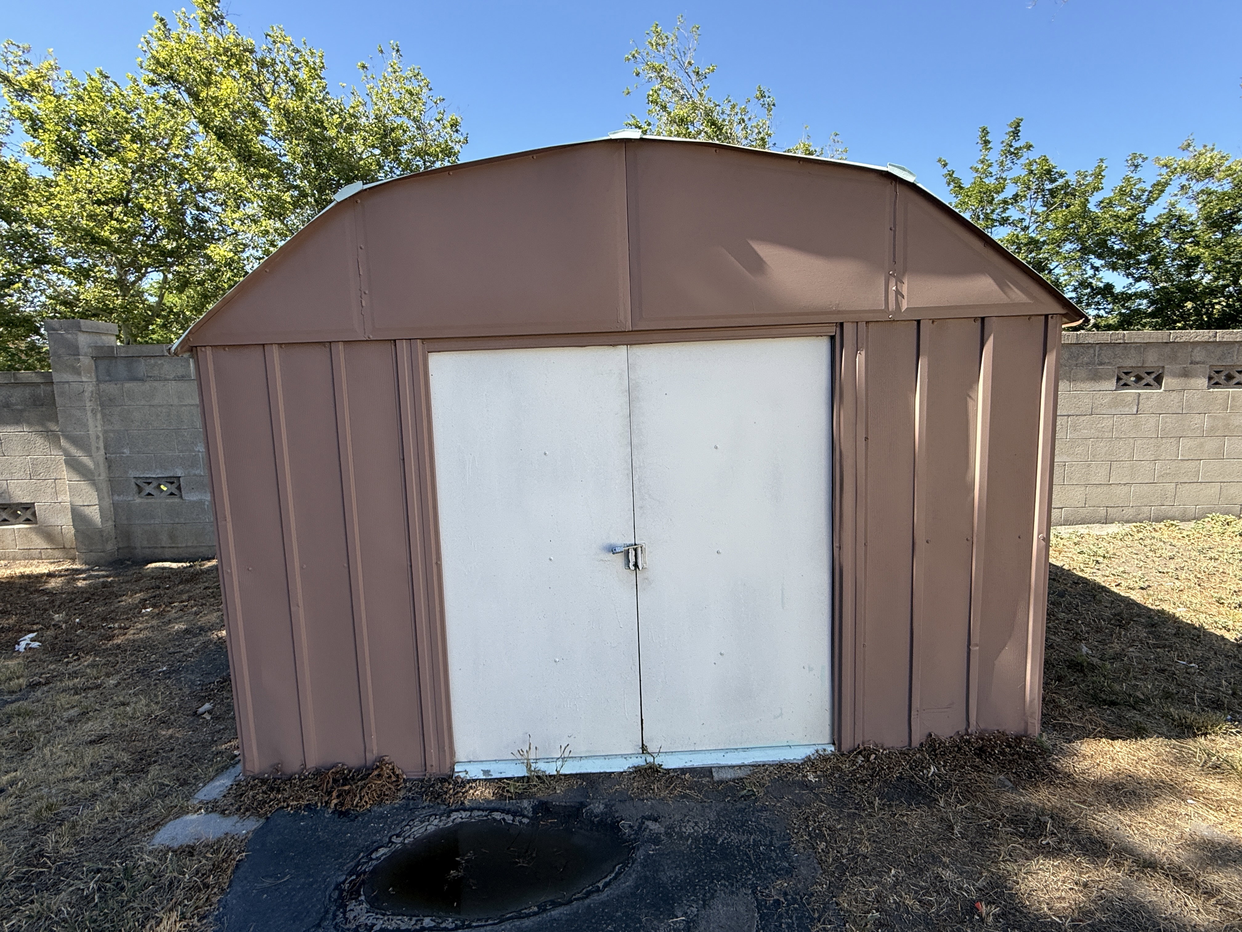 Brown metal shed with a barrel-vaulted roof and double white doors