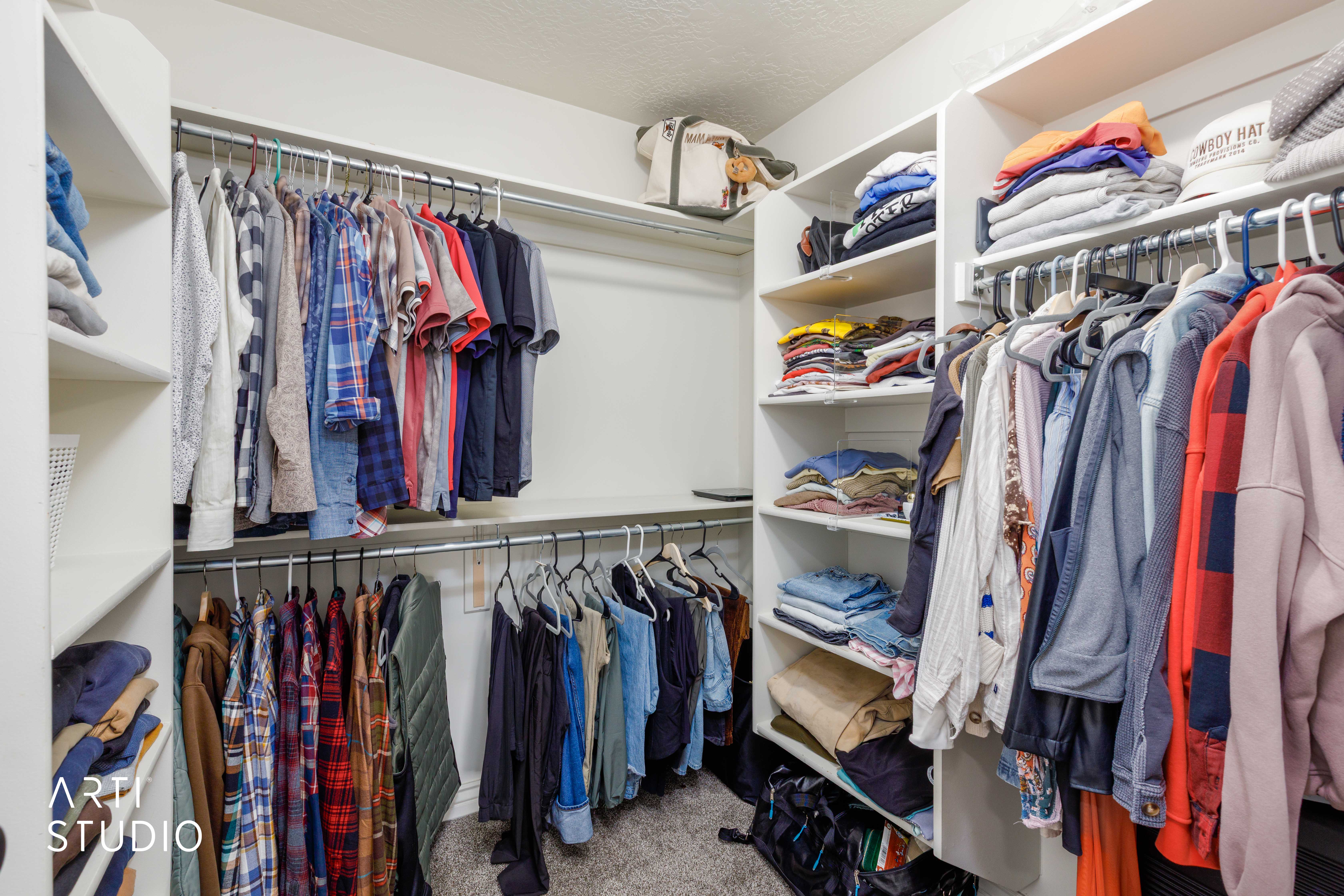 Walk-in closet featuring white built-in shelving, multiple hanging rods, and light gray carpeting