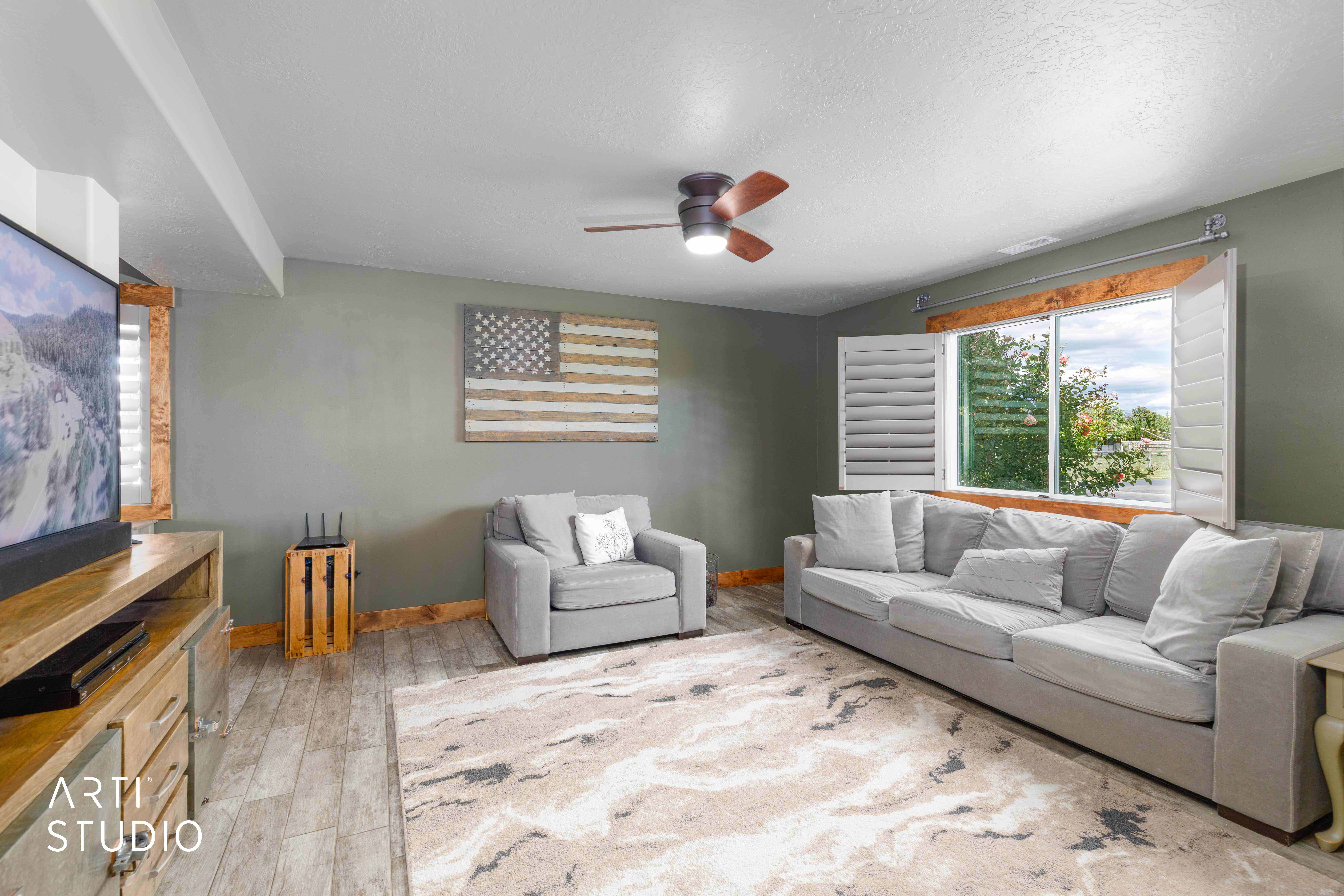 Spacious living area featuring tile flooring, a ceiling fan with integrated lighting, and a large window with plantation shutters