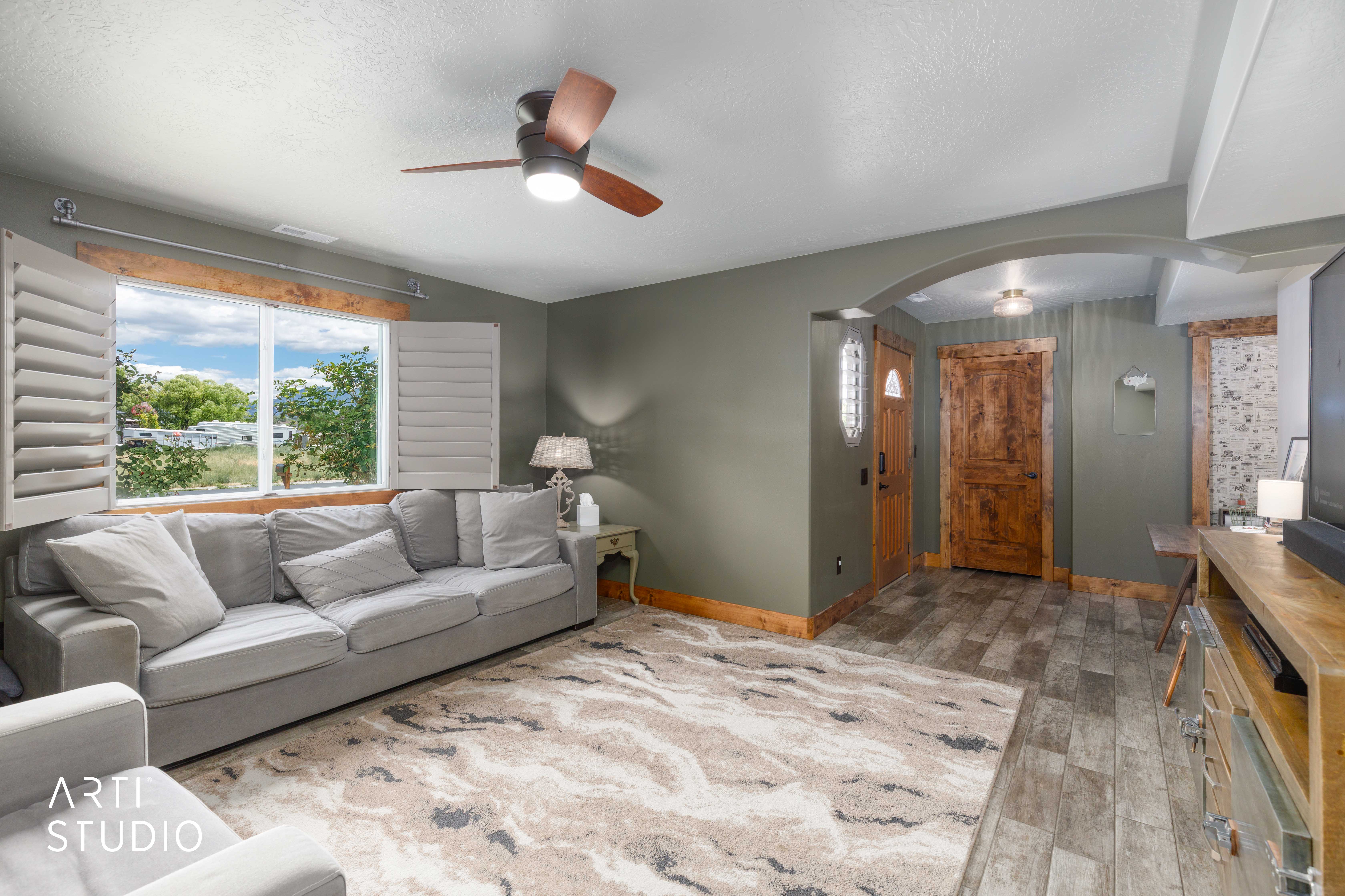 Spacious living area featuring a large window with plantation shutters, tile flooring, and a ceiling fan