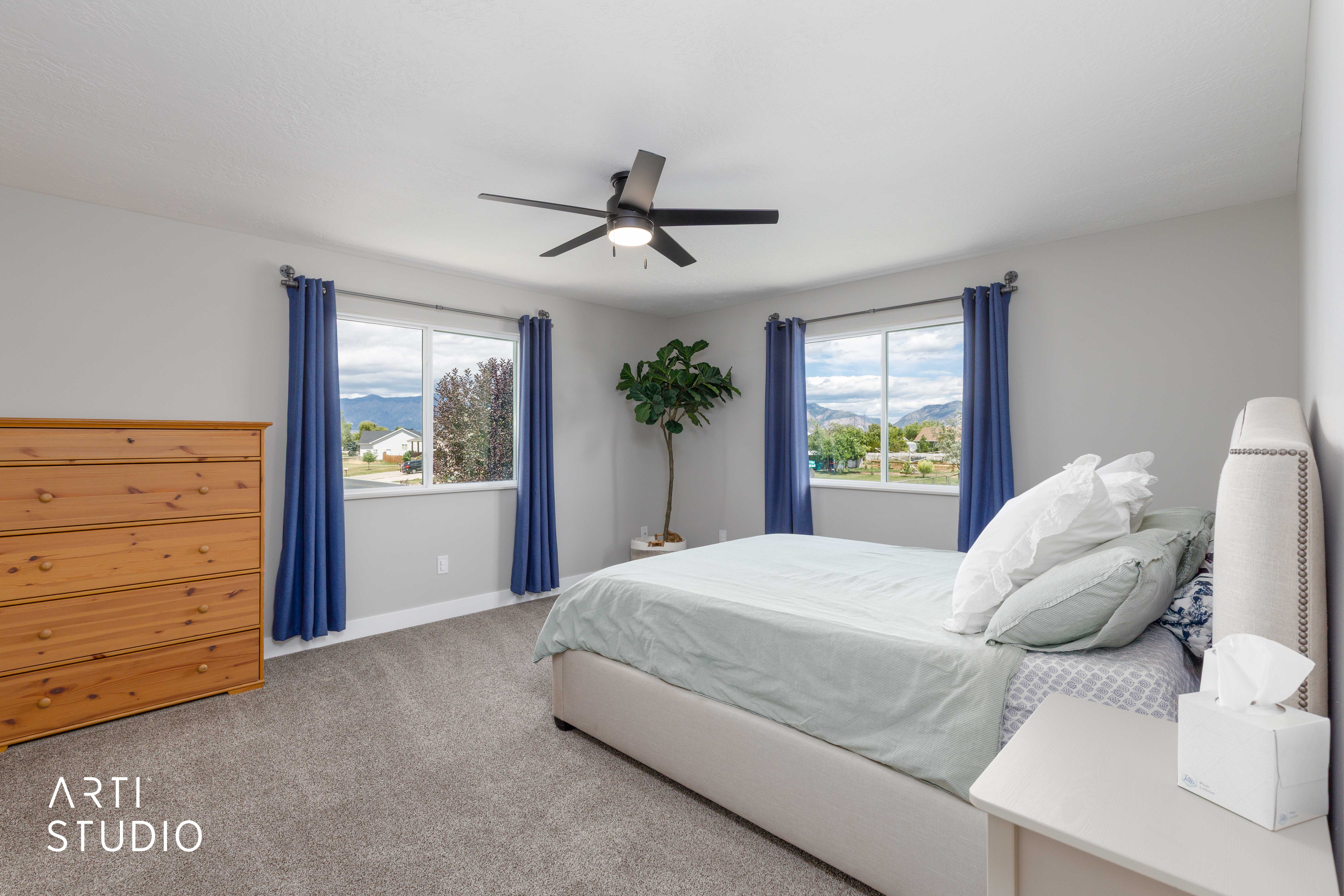 Spacious room featuring multiple windows, soft grey carpet flooring, a ceiling fan with light fixture, and light grey wall finishes