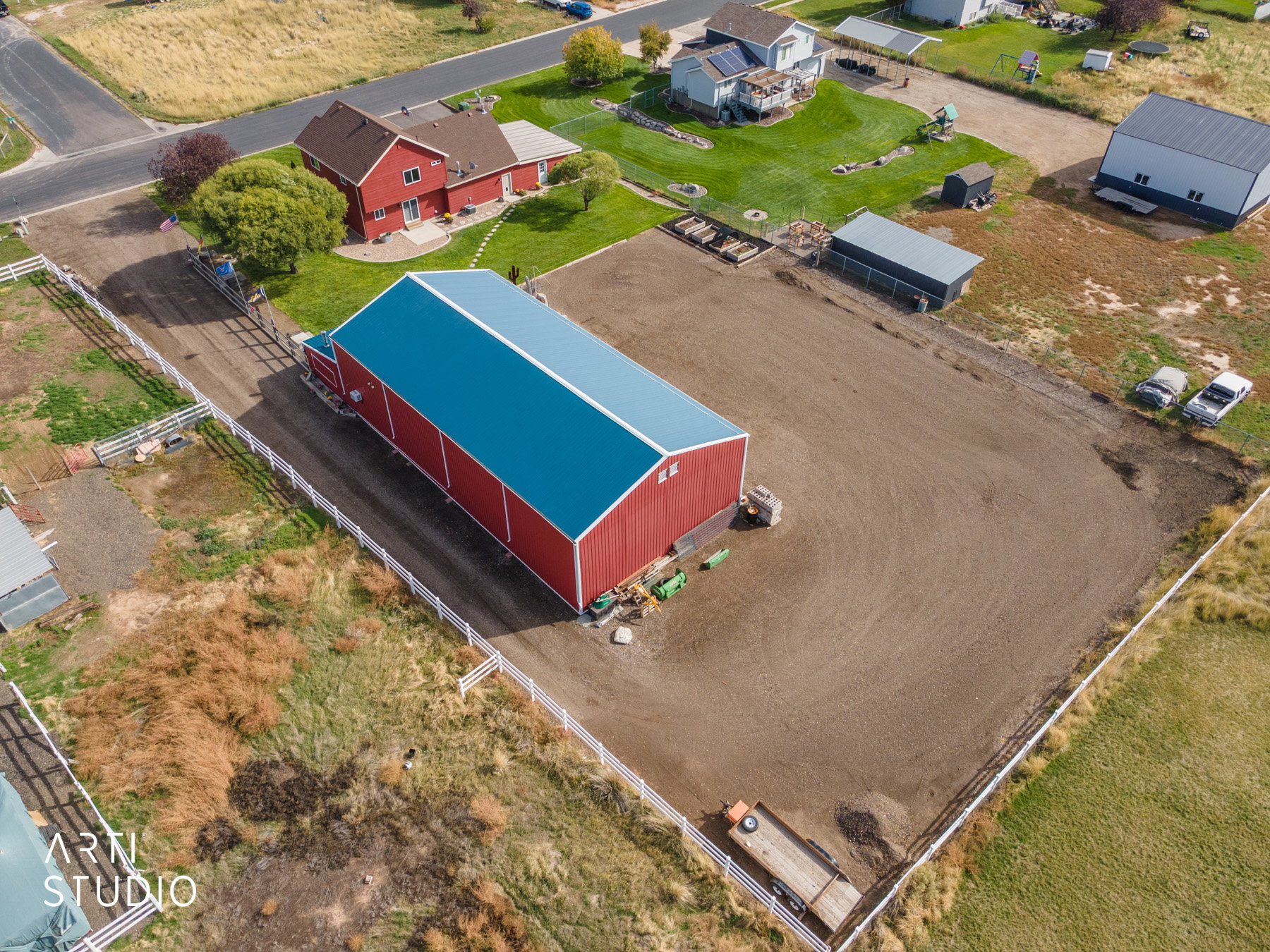 Spacious property featuring a large red barn with a blue metal roof, a red residential structure with a shingled roof, a substantial fenced lot