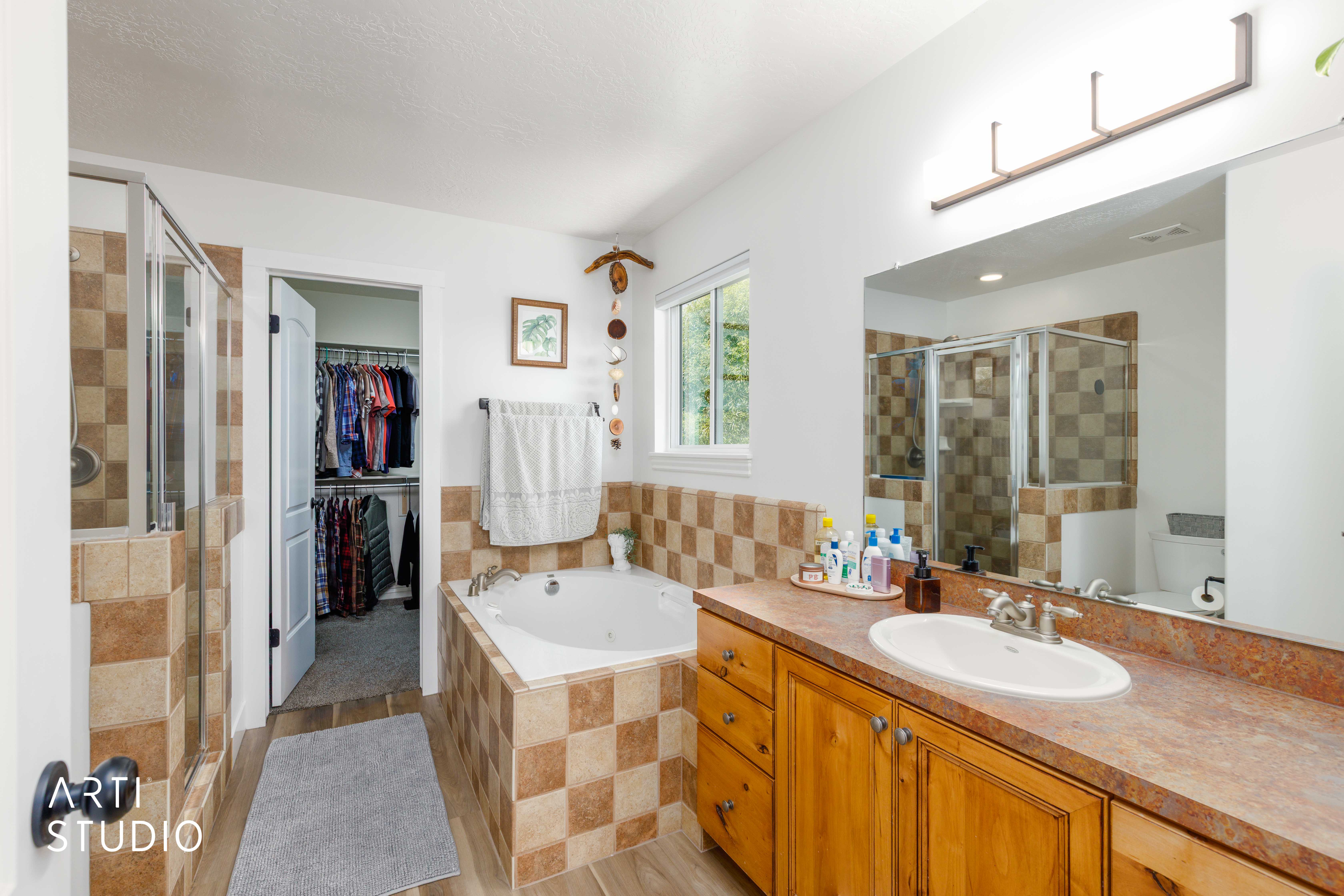 Bathroom featuring a built-in jetted tub with checkerboard tile surround, a separate glass-enclosed shower with matching tile, and a wood-finish vanity with an integrated sink