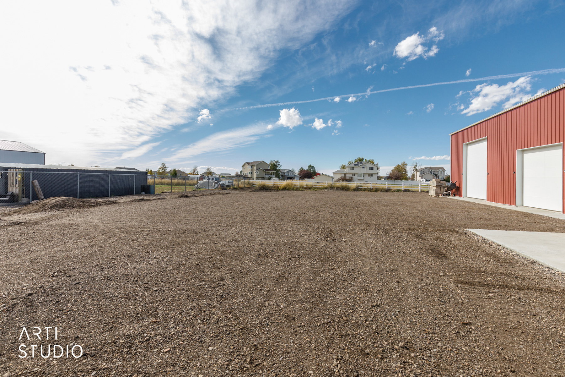 Expansive cleared lot featuring a red metal building with two large roll-up doors, and a concrete pad