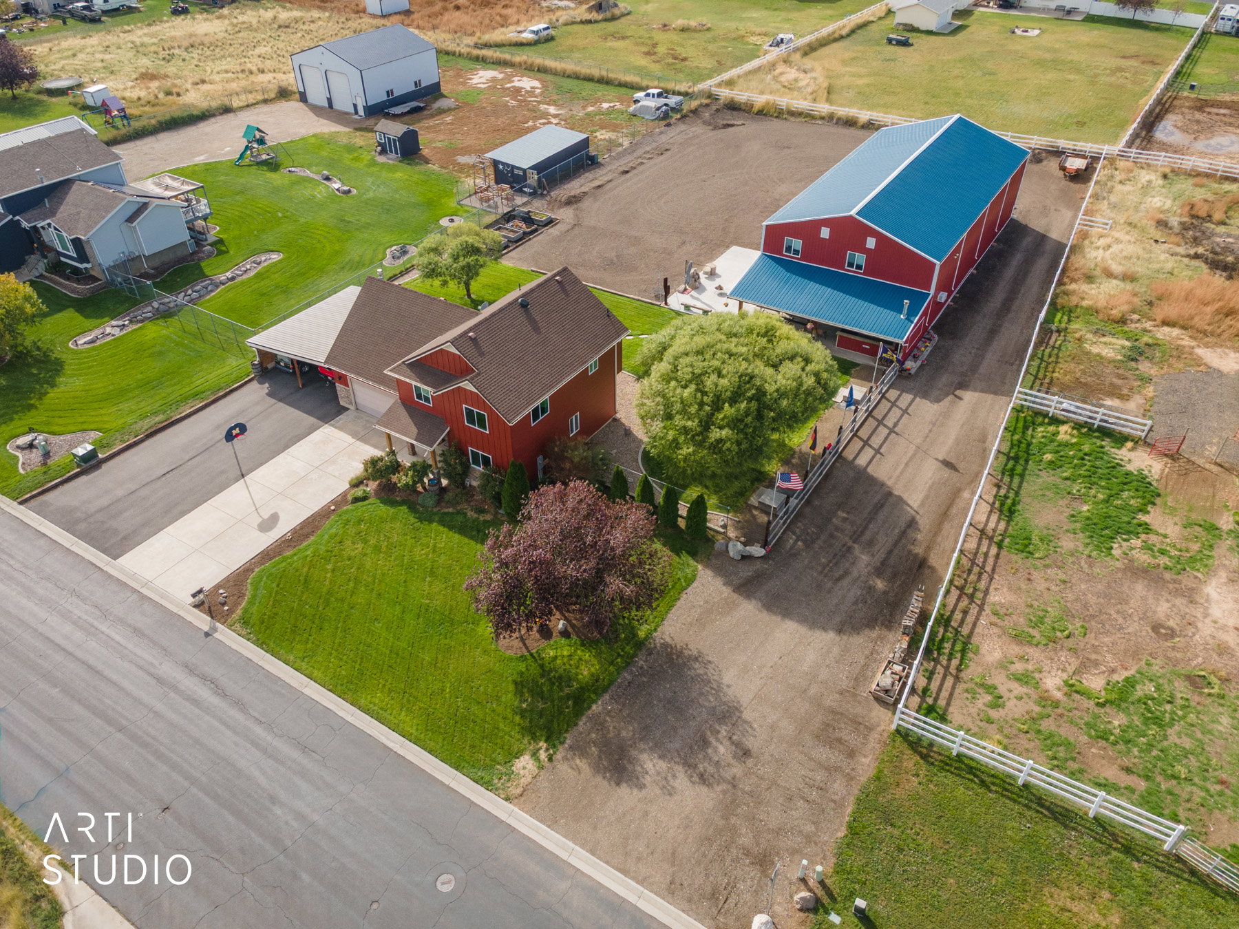 Red two-story residence featuring a carport and attached garage, mature landscaping, and an expansive paved driveway