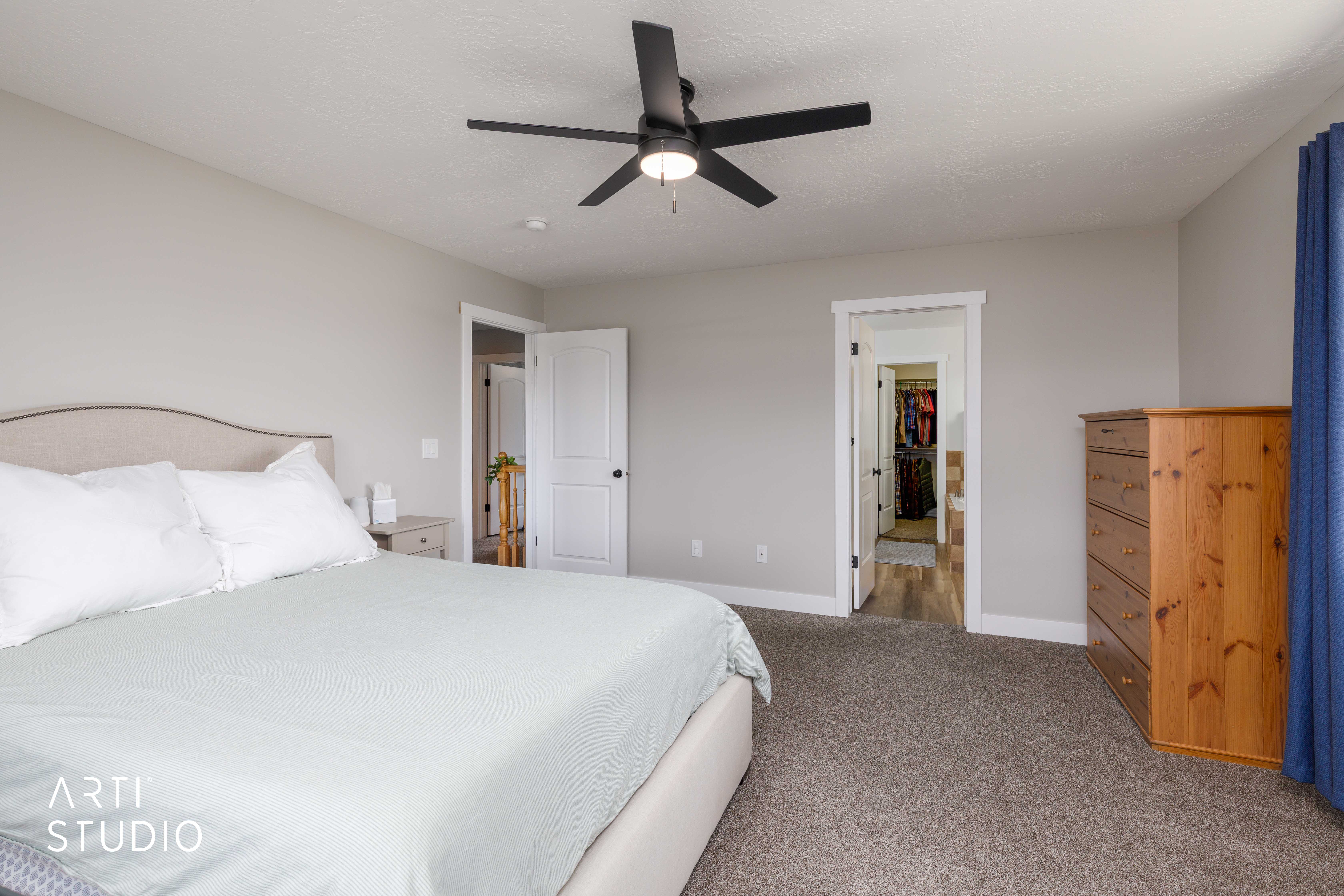 Spacious room with light gray walls, dark gray carpet, a black ceiling fan, white trim, and a white interior door