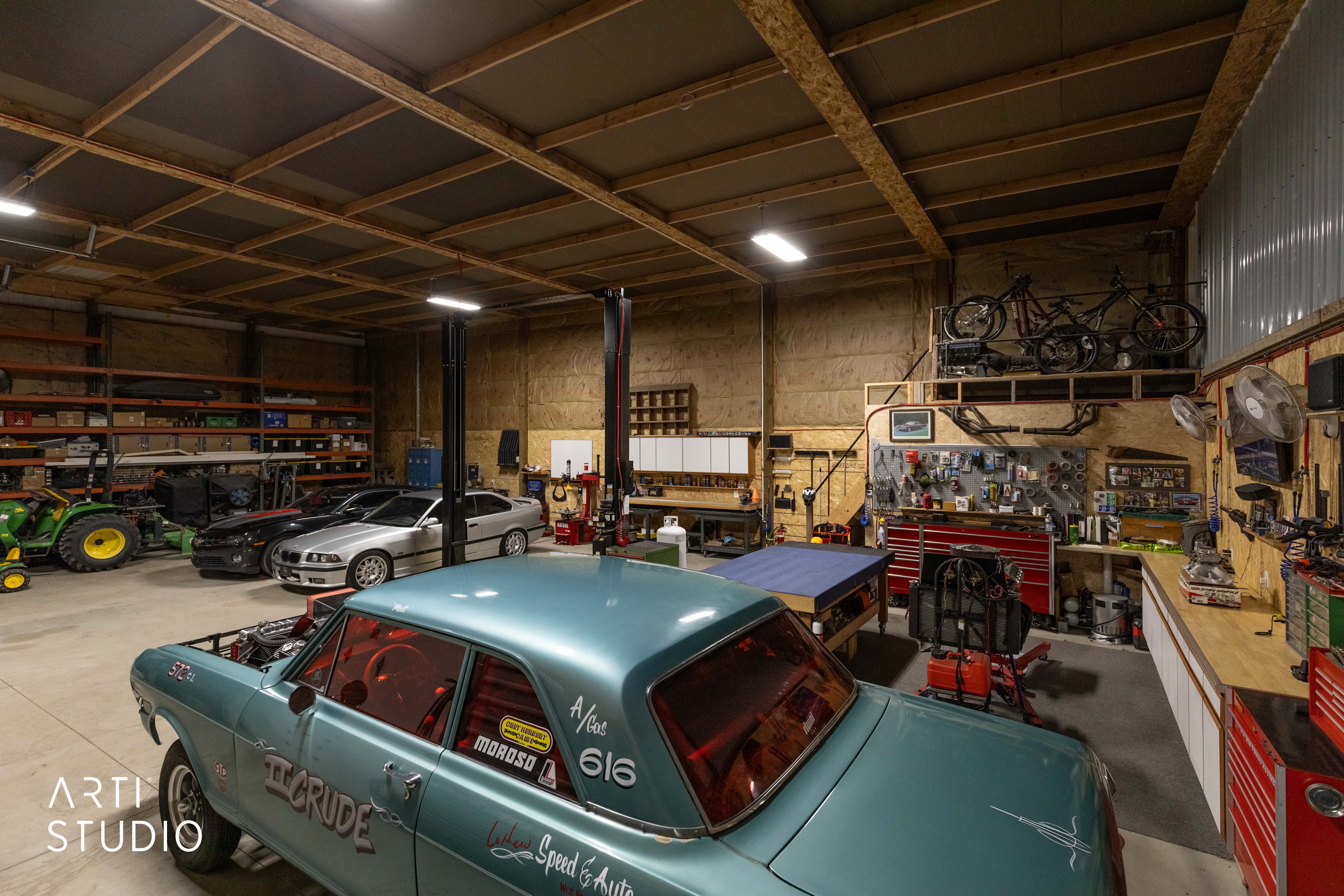 Spacious utility garage featuring exposed wood beam ceiling, concrete flooring, built-in shelving, two vehicle lifts, and extensive workbench areas