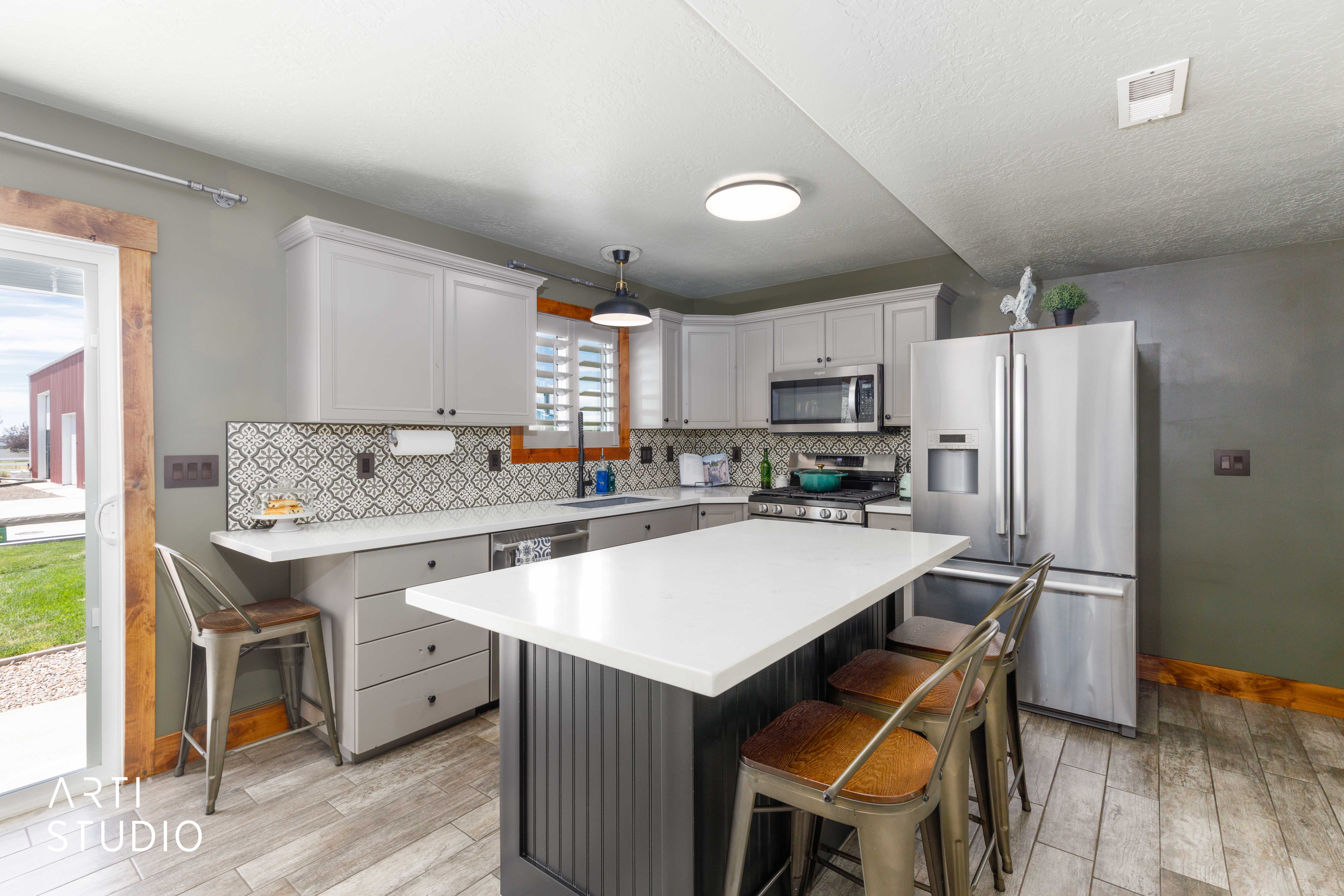 Kitchen featuring light gray cabinetry, stainless steel appliances, a patterned tile backsplash, tile flooring, and a central island with a white countertop