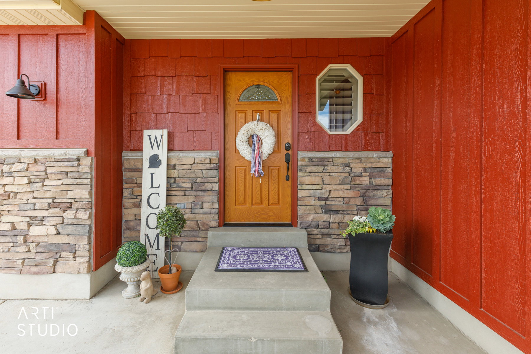 Entryway featuring a wood-finish door with decorative glass, flanked by red siding and natural stone accents