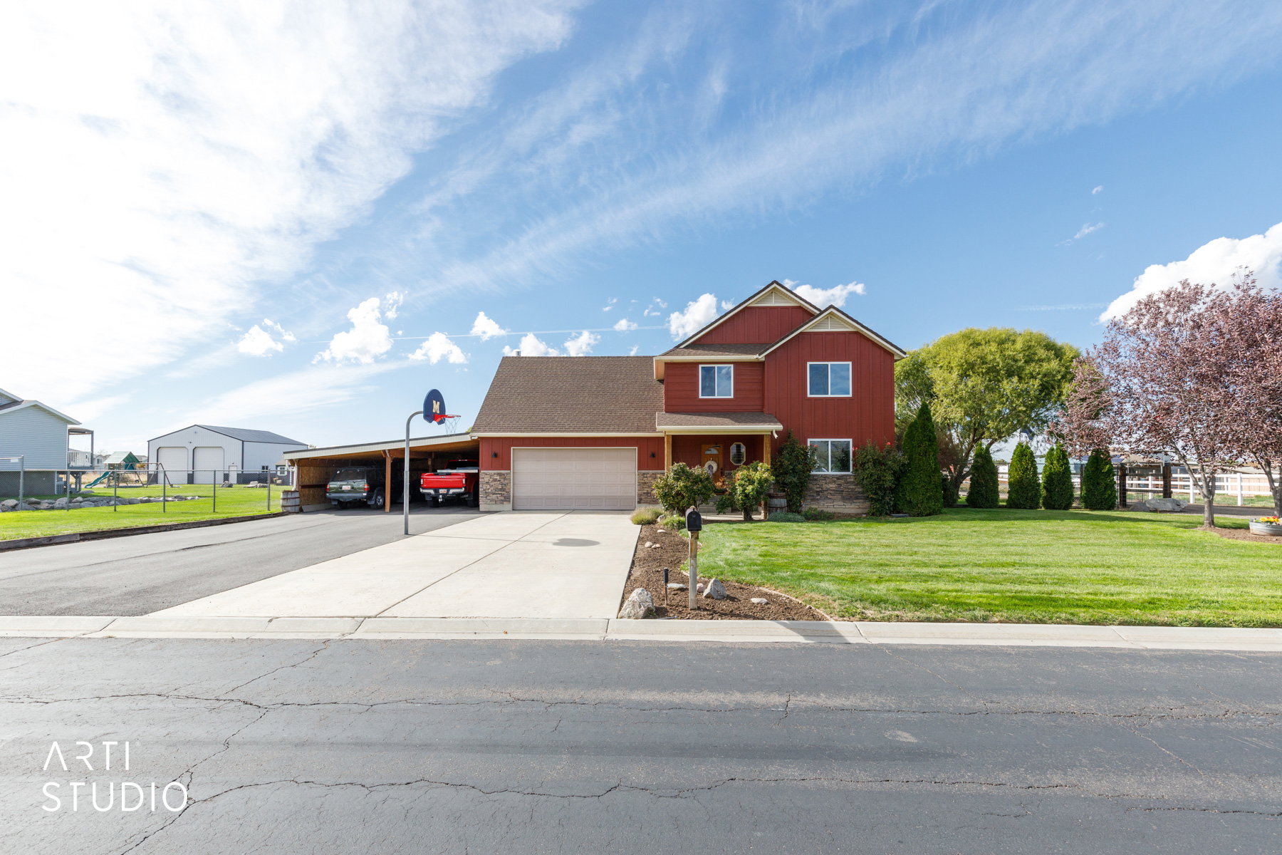Red siding exterior with stone accents, a double-car garage, and an attached carport