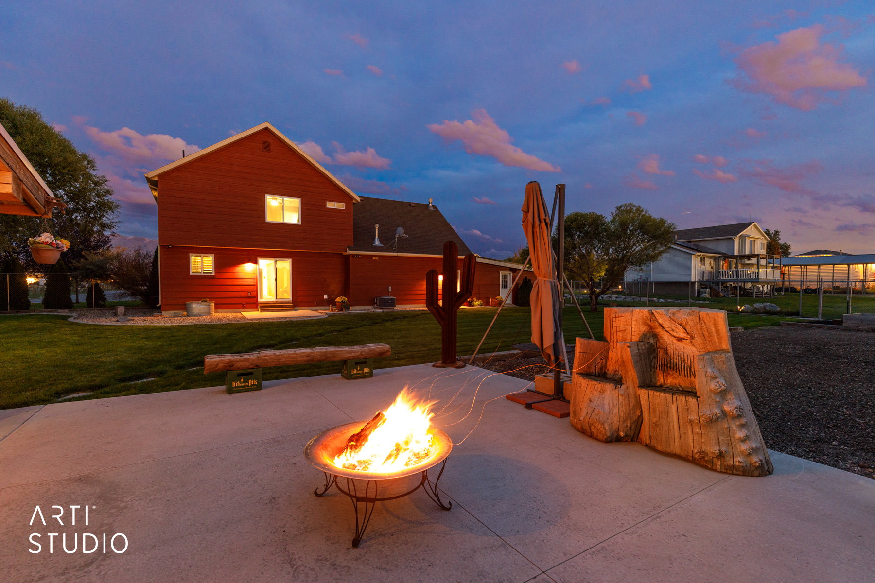 Rear exterior featuring a concrete patio with a fire pit, mature landscaping, and a red siding facade with a sliding glass door