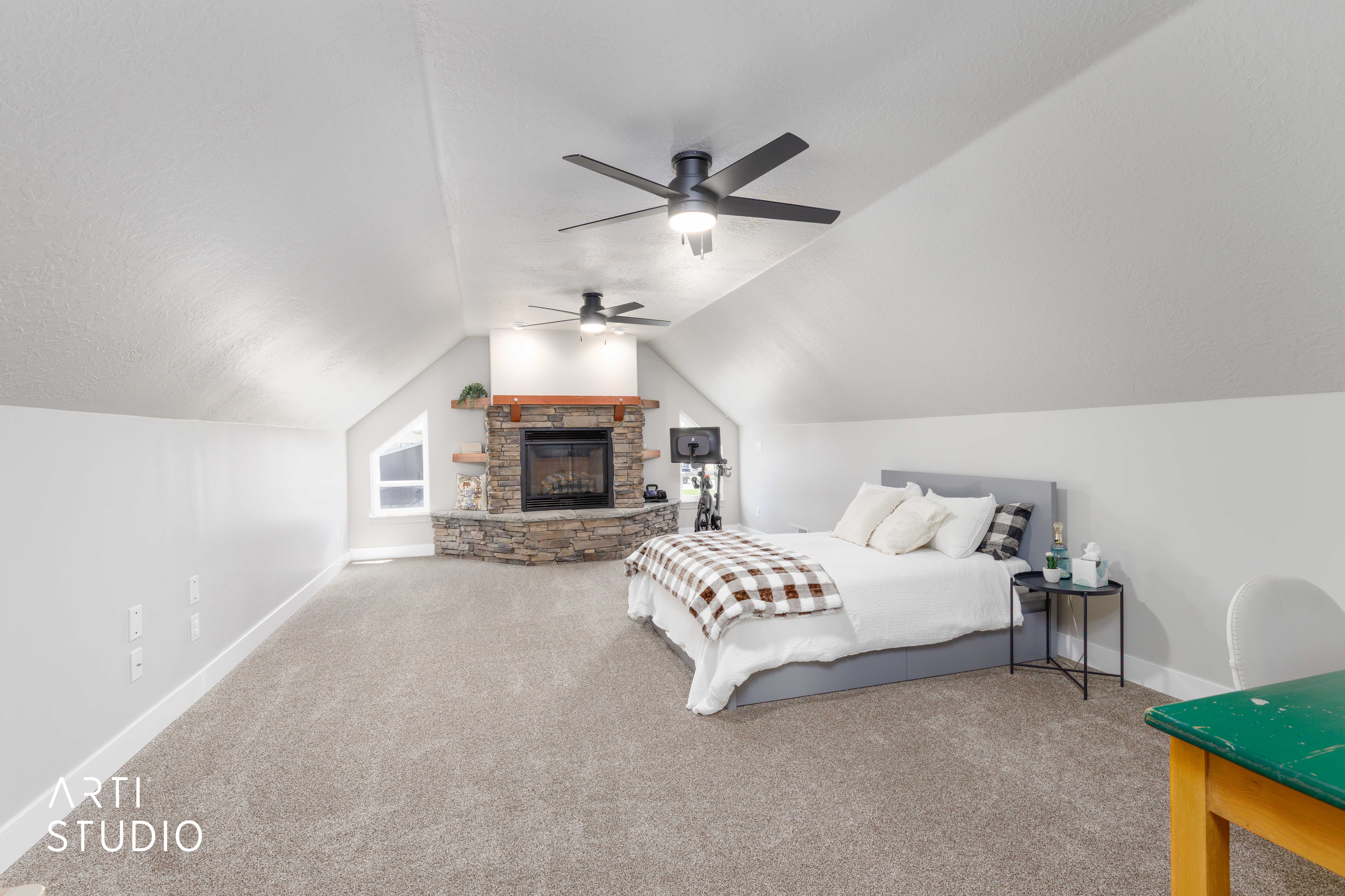 Spacious room featuring a corner stone fireplace with wood mantel, vaulted ceilings, two ceiling fans, and neutral-toned carpeting