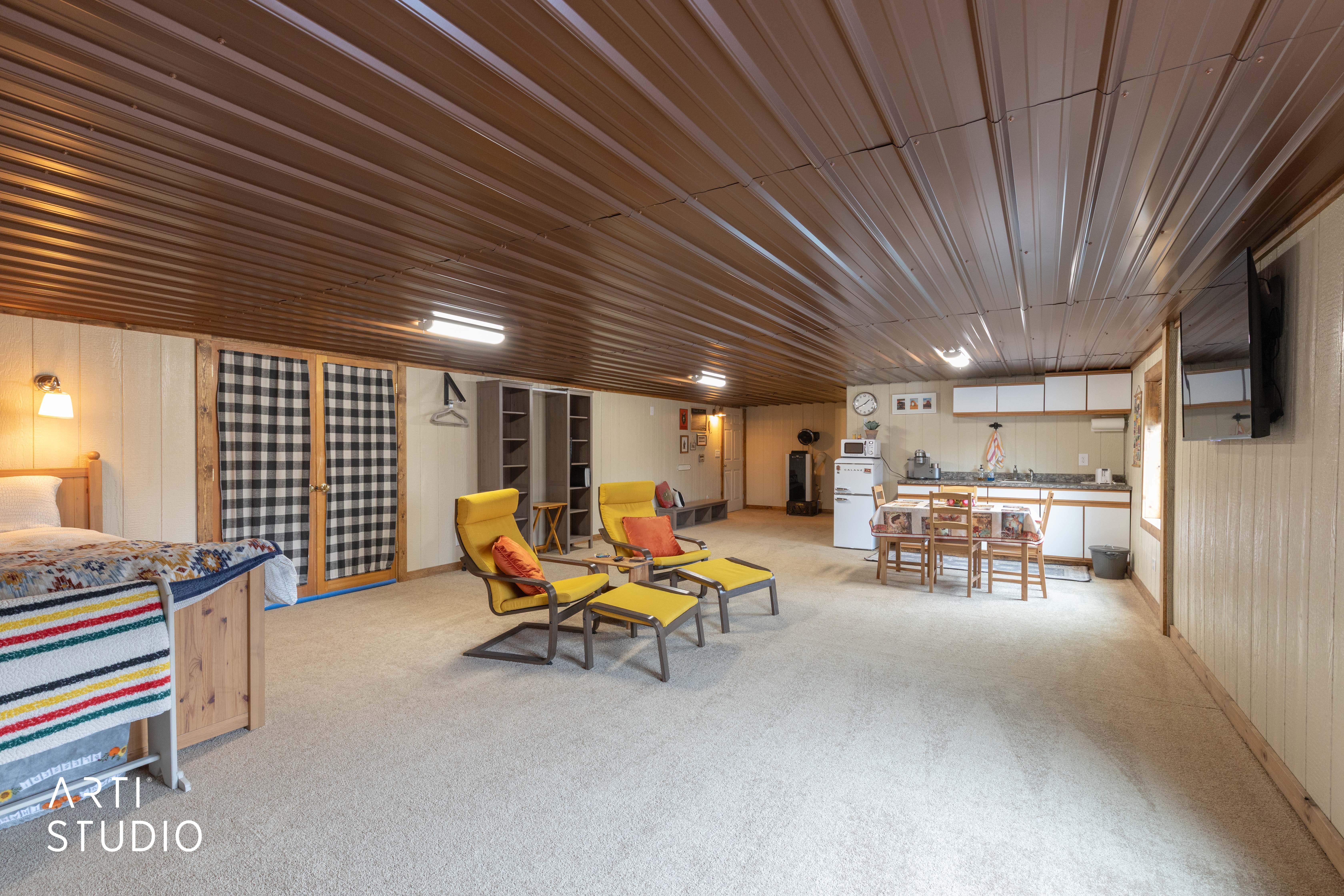Open concept area featuring a compact kitchen, carpeted flooring, and a corrugated metal ceiling