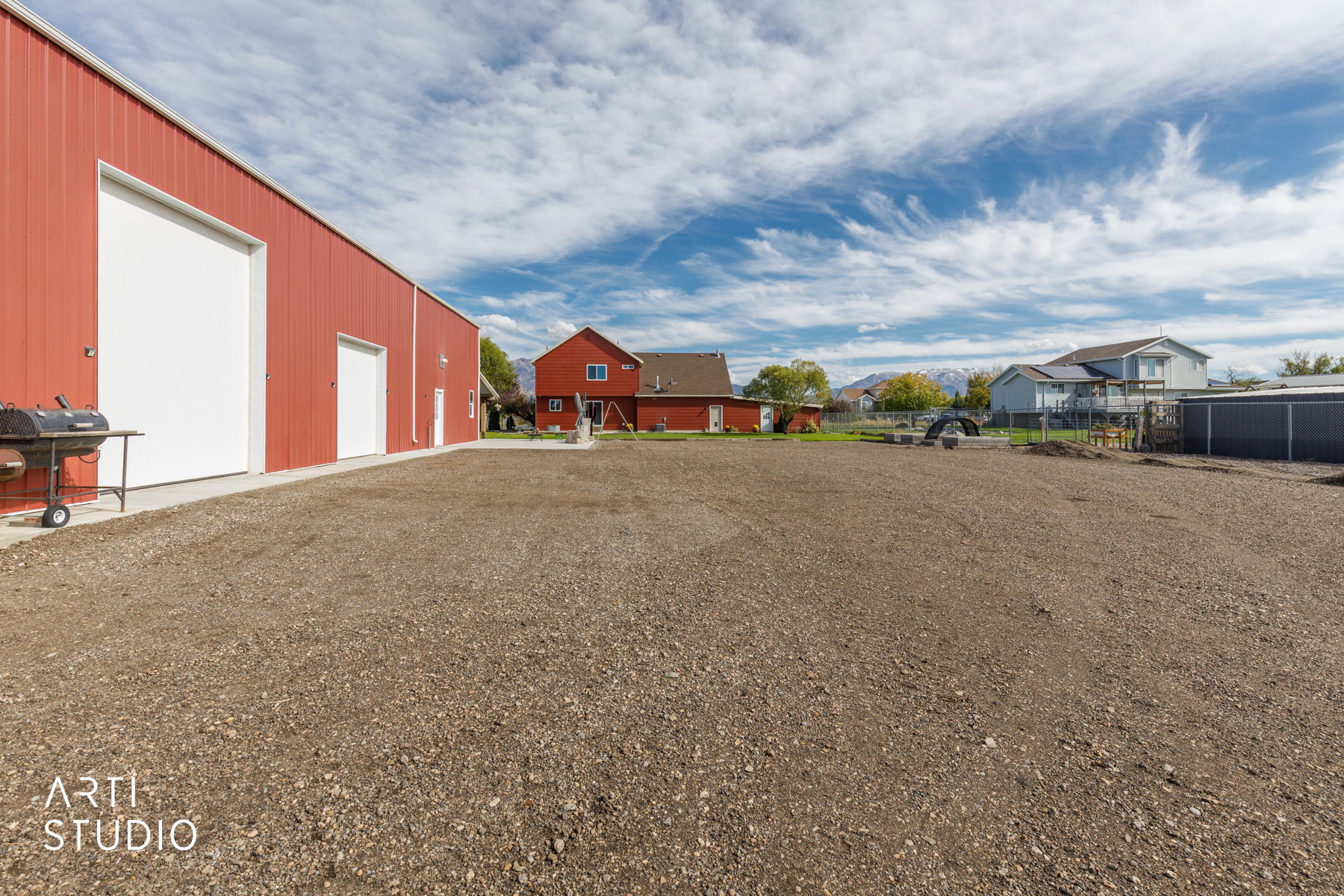 Expansive gravel lot with a red metal building featuring two large roll-up doors and a pedestrian door