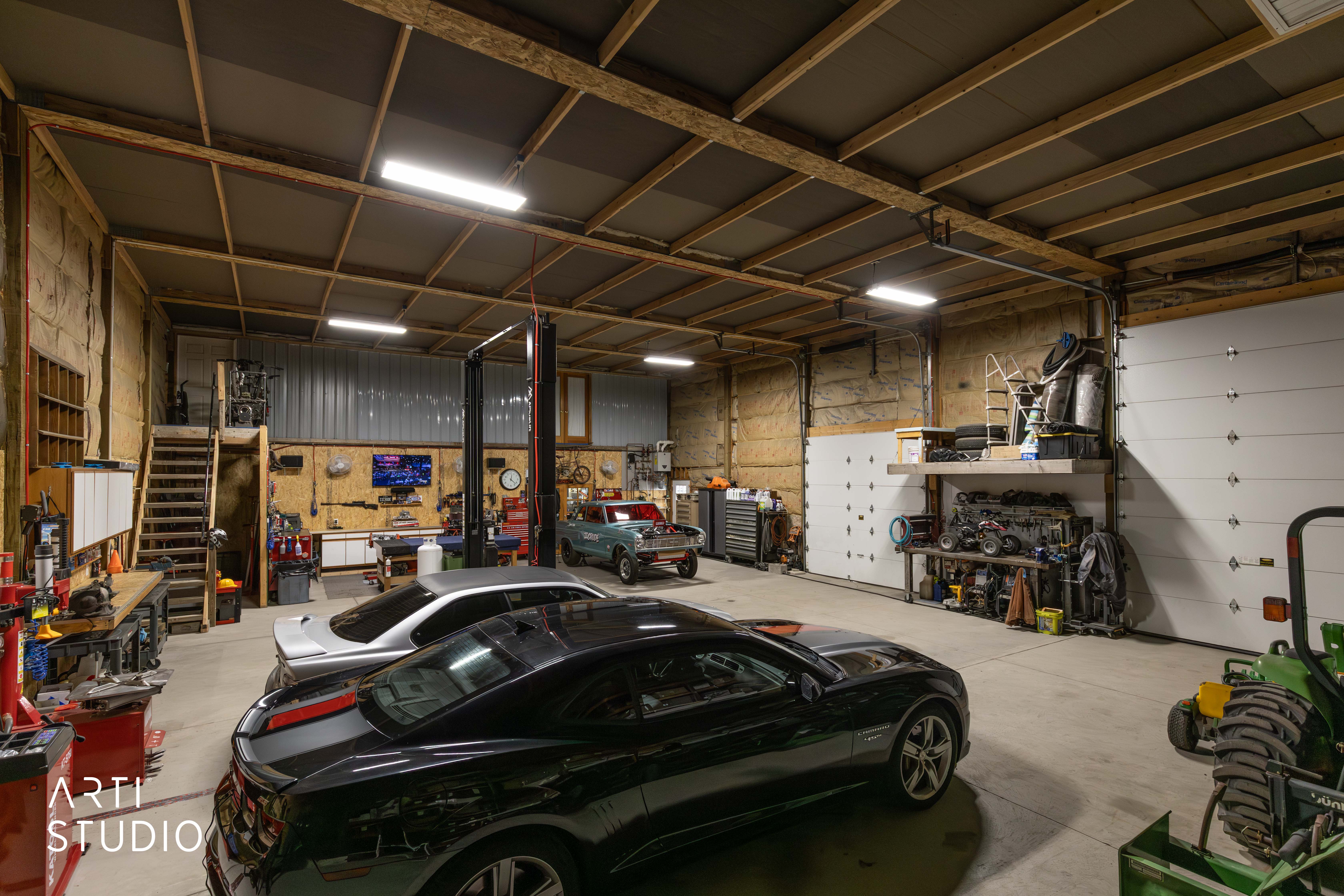 Spacious garage featuring high ceilings with exposed wood framing, concrete flooring, multiple overhead fluorescent lights, and a vehicle lift
