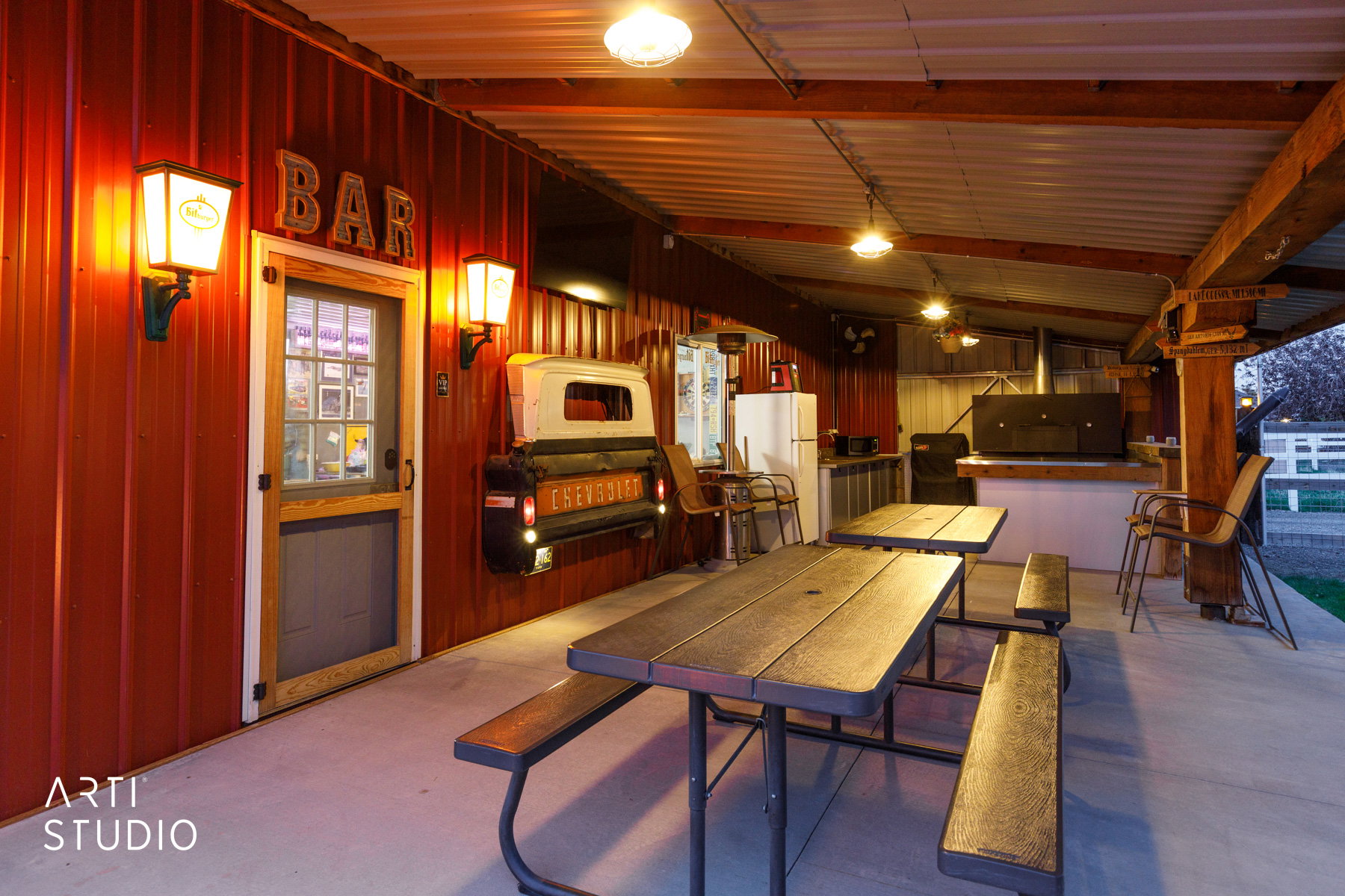 Covered outdoor entertaining area featuring a red corrugated metal wall, a built-in outdoor kitchen with a large grill, and a concrete patio