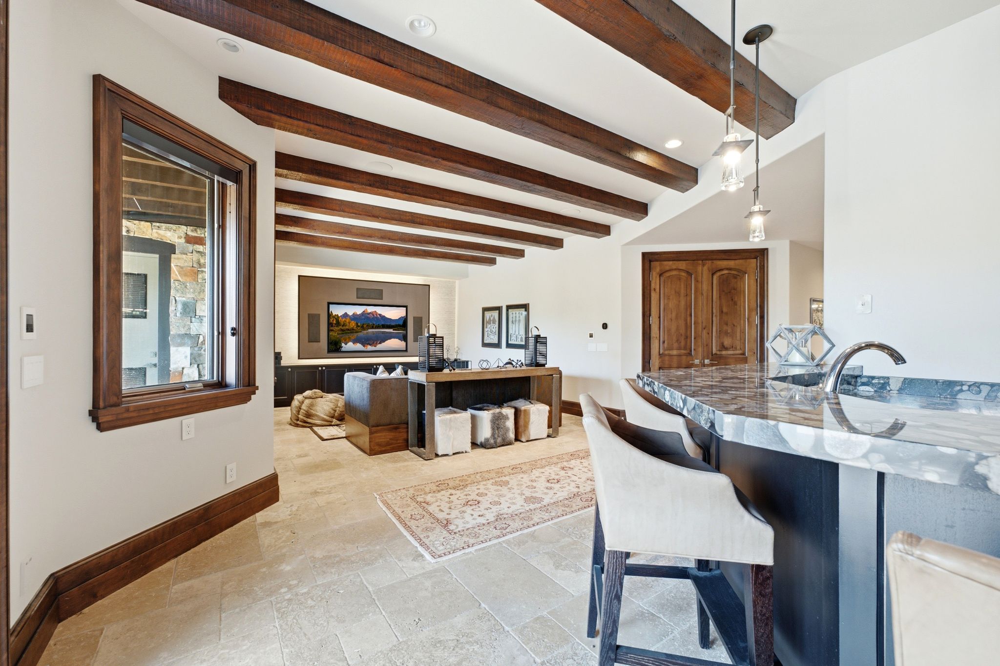 Open entertainment space featuring a built-in media wall, stone tile flooring, and exposed wood ceiling beams