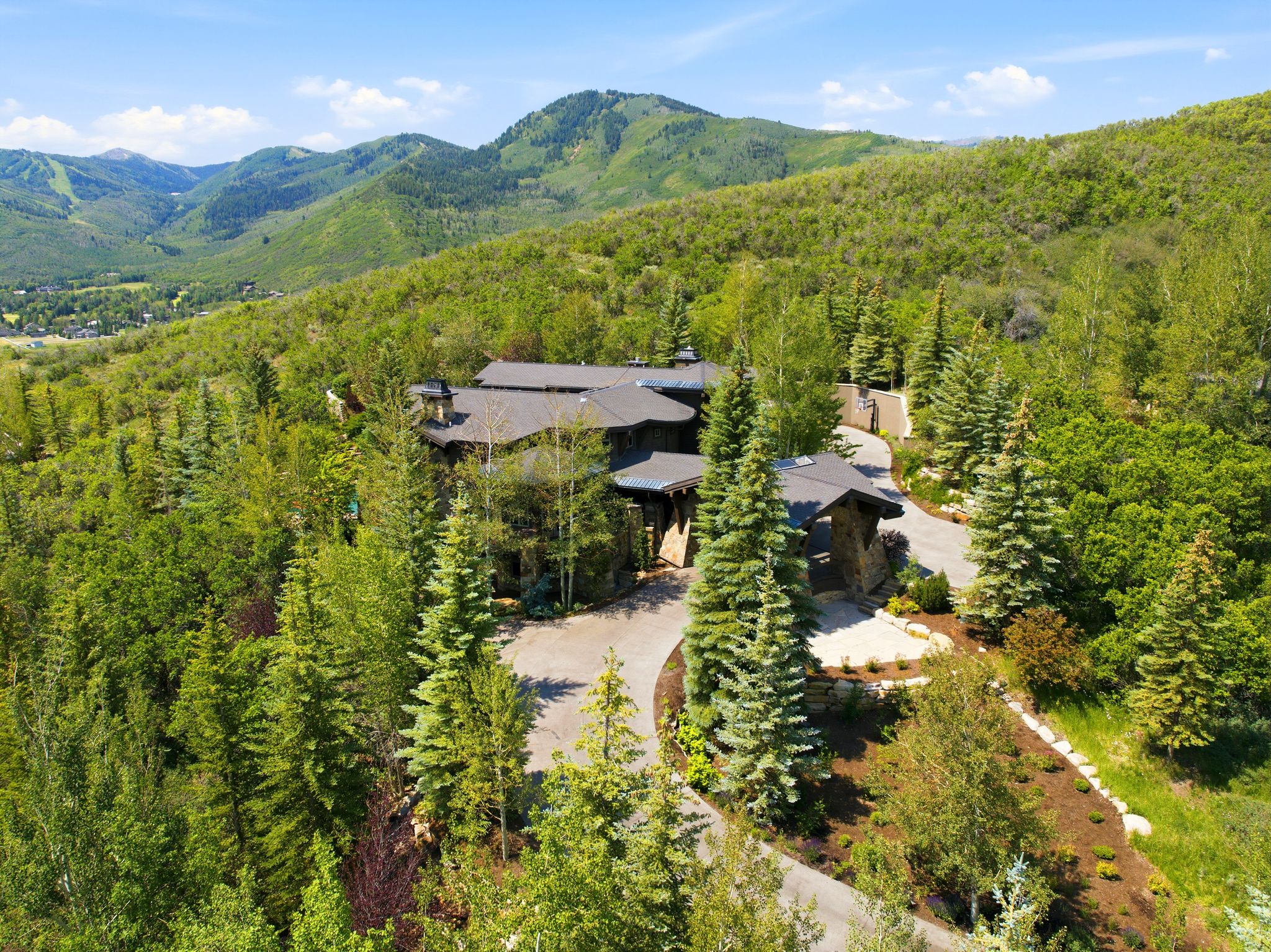 Architectural residence nestled amongst mature trees, featuring a stone and wood facade, multiple rooflines, and a paved circular driveway
