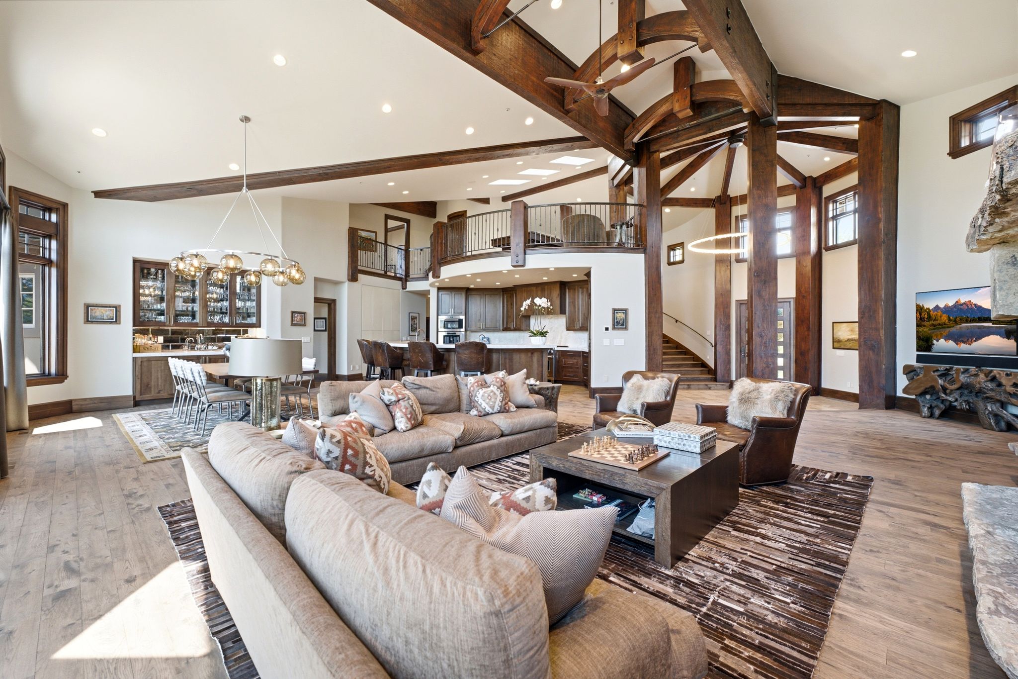 Expansive living area featuring vaulted ceilings with exposed wood beams, wood-finish flooring, a stone-clad fireplace, and a built-in dining area with extensive cabinetry