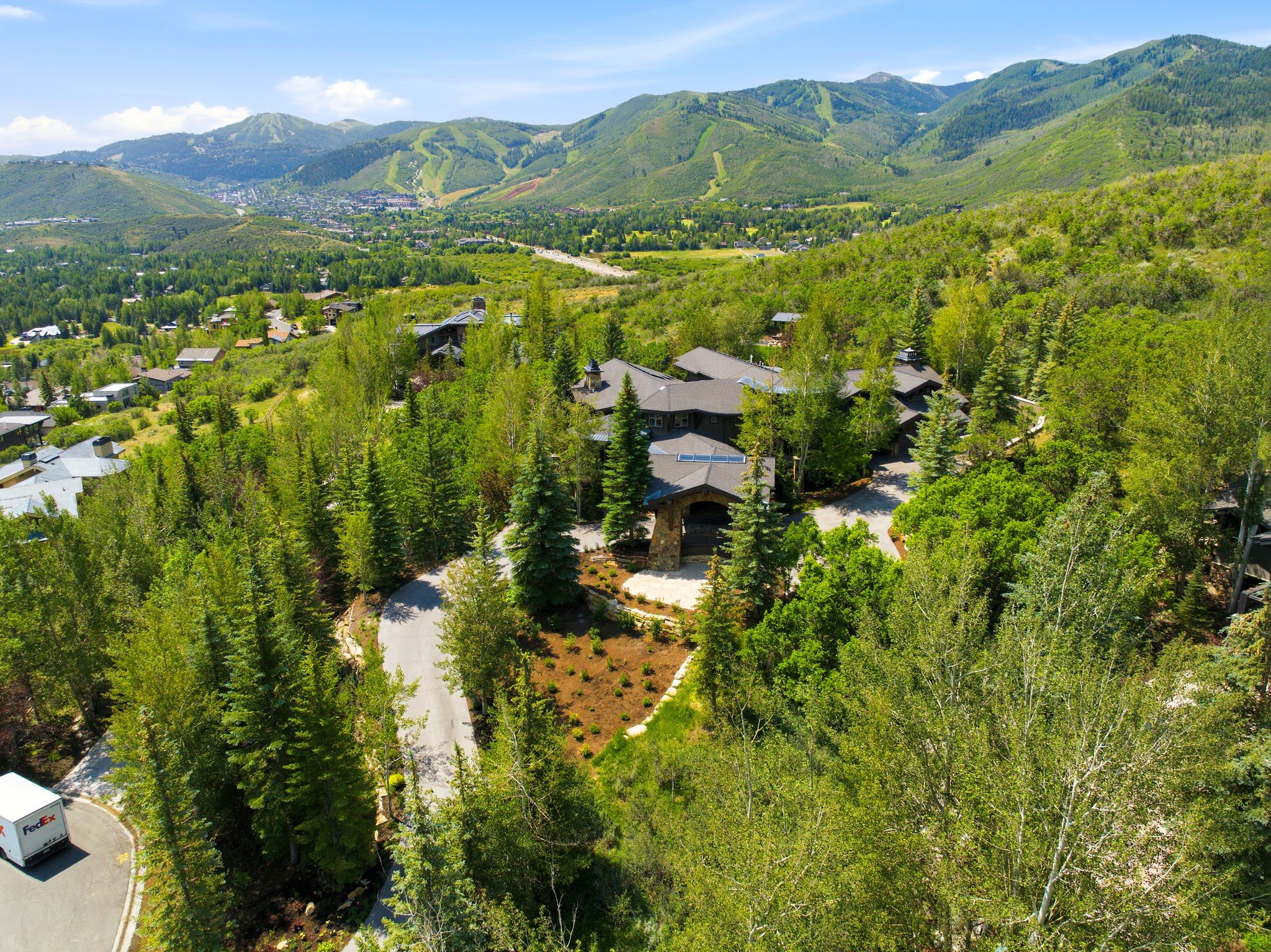 Expansive property featuring a stone and wood exterior, multiple rooflines, a private driveway, and mature landscaping, all set against a mountainous backdrop