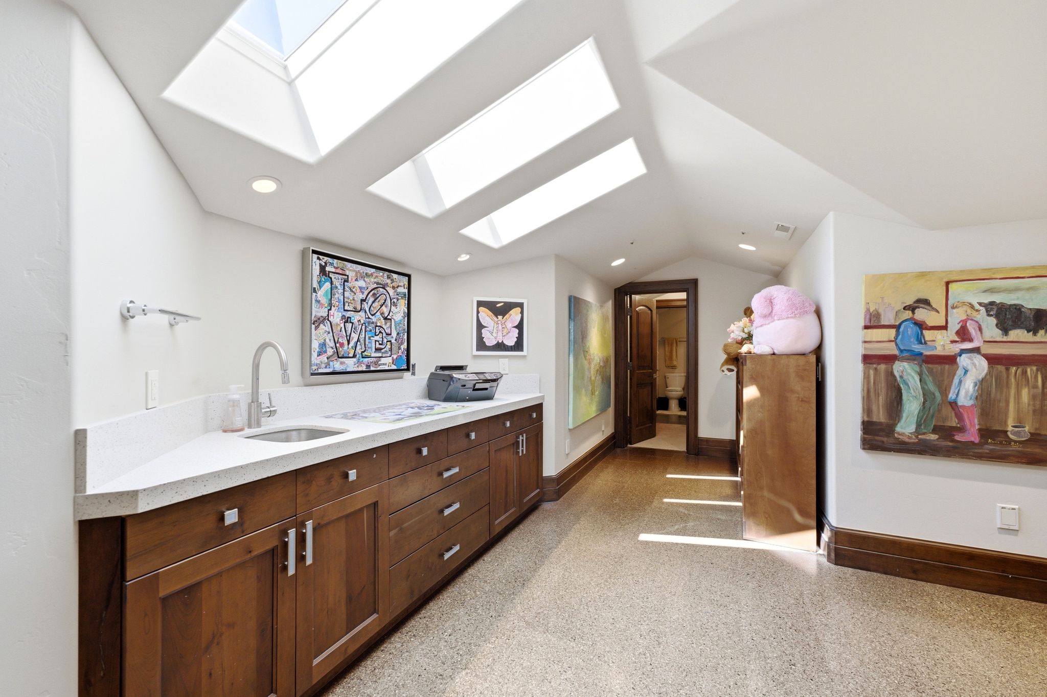 Atrium-style skylights illuminate this versatile space featuring a built-in countertop with an undermount sink, wood cabinetry, and recessed lighting