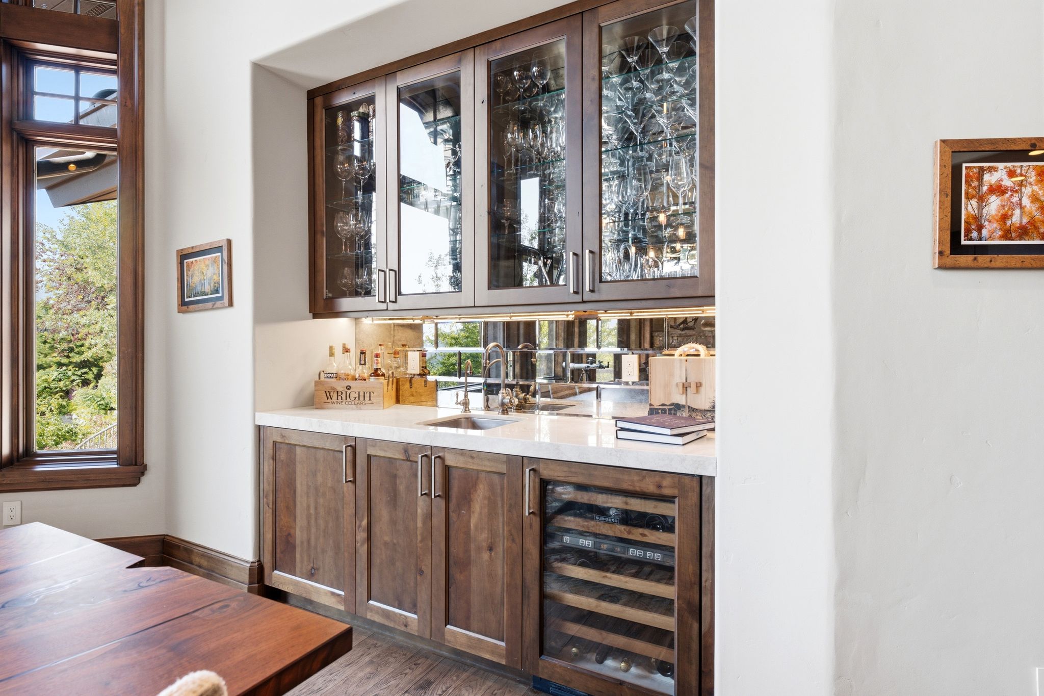 Built-in wet bar featuring upper glass-front cabinetry, a mirrored backsplash, undermount sink, and a wine refrigerator