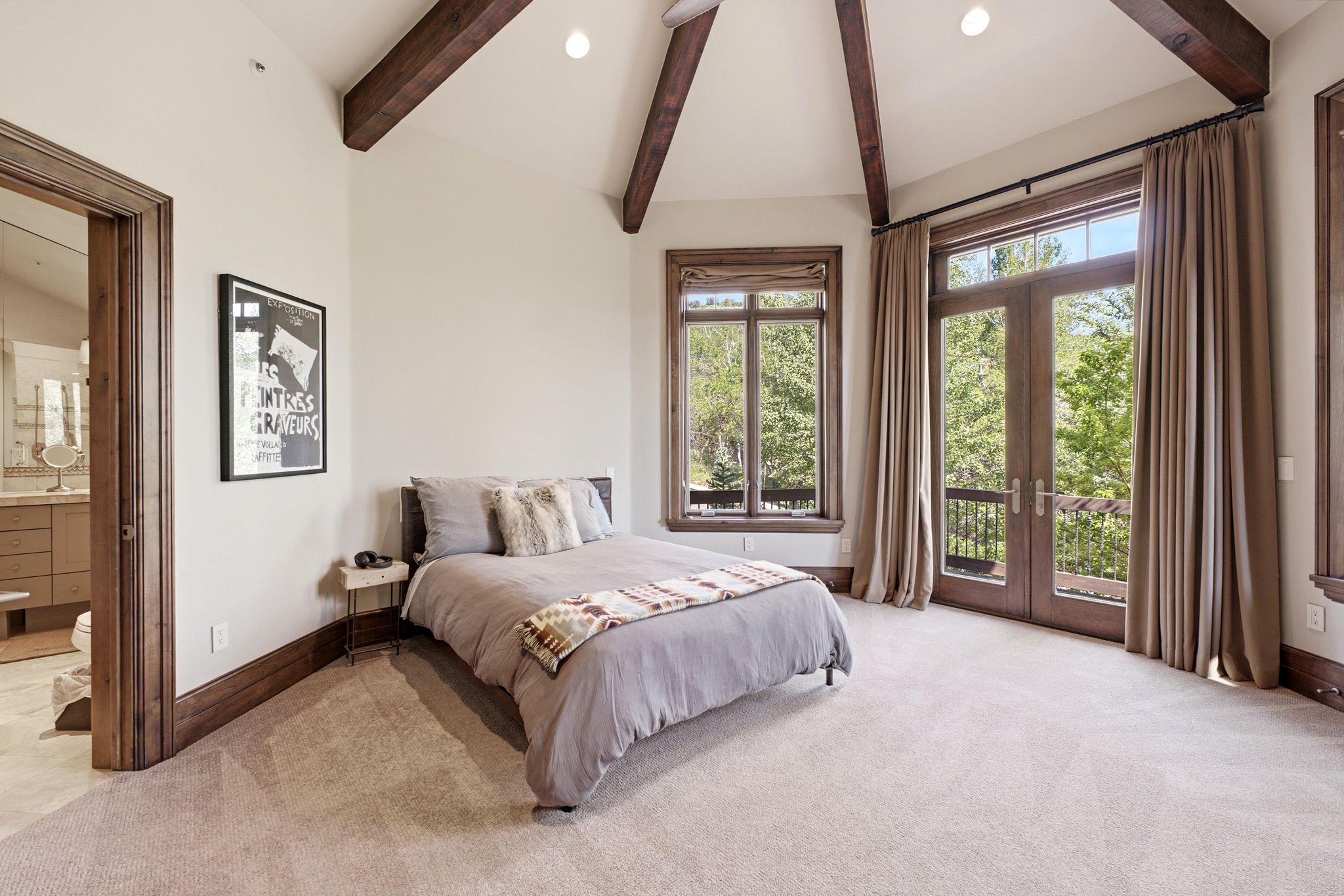 Vaulted ceiling with exposed wood beams, French doors opening to an exterior balcony, wood-framed windows, recessed lighting, and plush carpet flooring