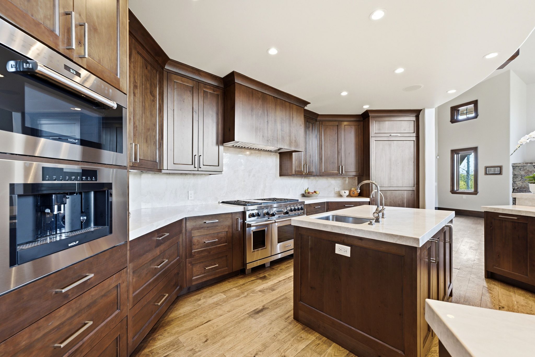Gourmet kitchen featuring rich wood cabinetry, light countertops, stainless steel appliances, a built-in coffee system, and wood-finish flooring