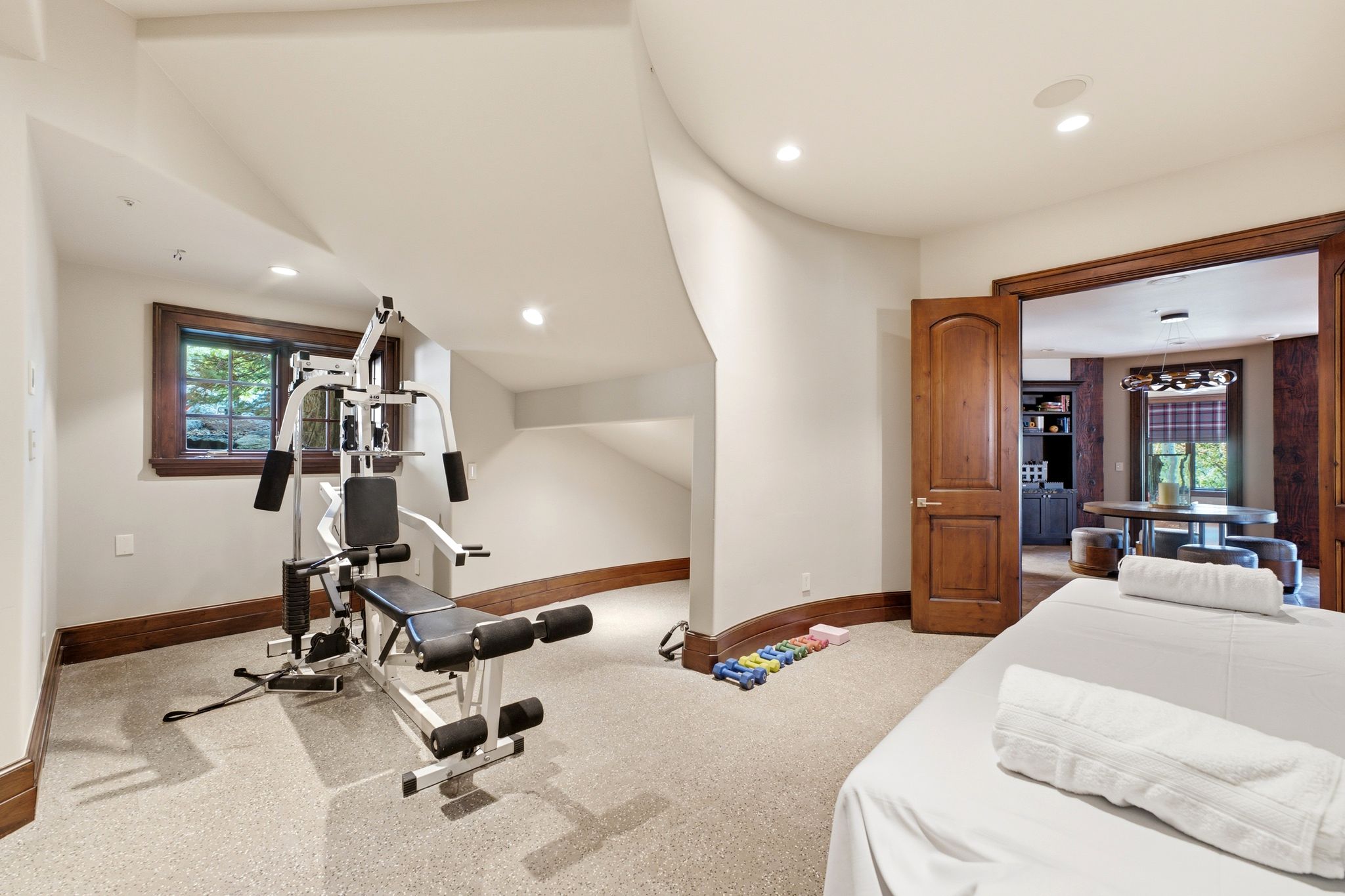Carpeted recreation room featuring a window with dark wood trim, recessed lighting, and a wood-paneled doorway opening into another room