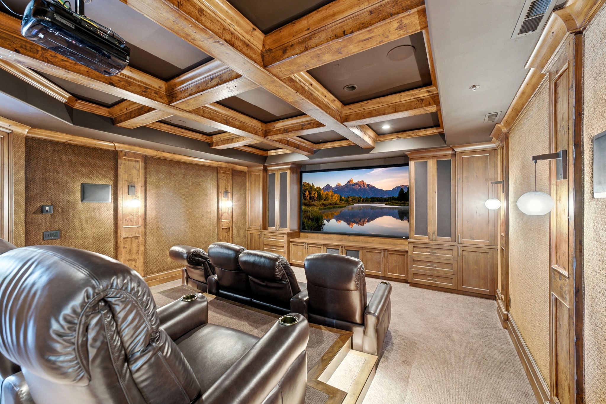 Dedicated media room featuring wood-finish coffered ceilings, wall paneling, built-in cabinetry, and integrated sconce lighting