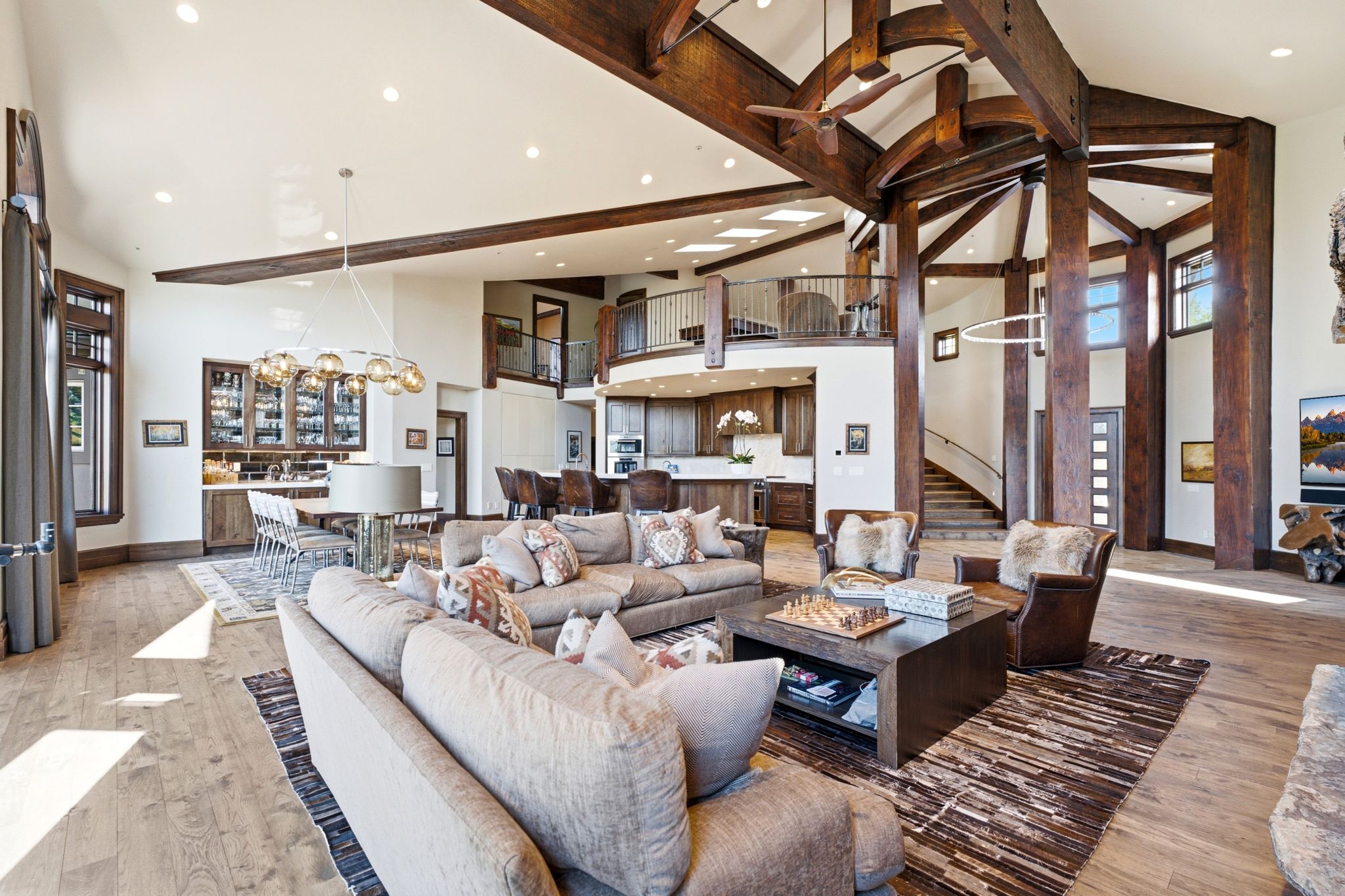 Grand living space featuring vaulted ceilings with exposed wood beams, hardwood flooring, and a second-story balcony