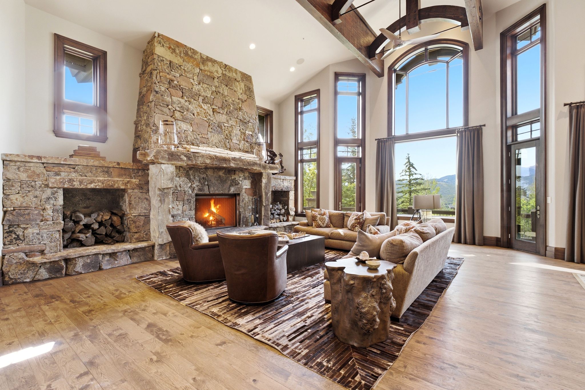 Great room featuring a floor-to-ceiling stone fireplace, high vaulted ceilings with exposed wood beams, and expansive windows