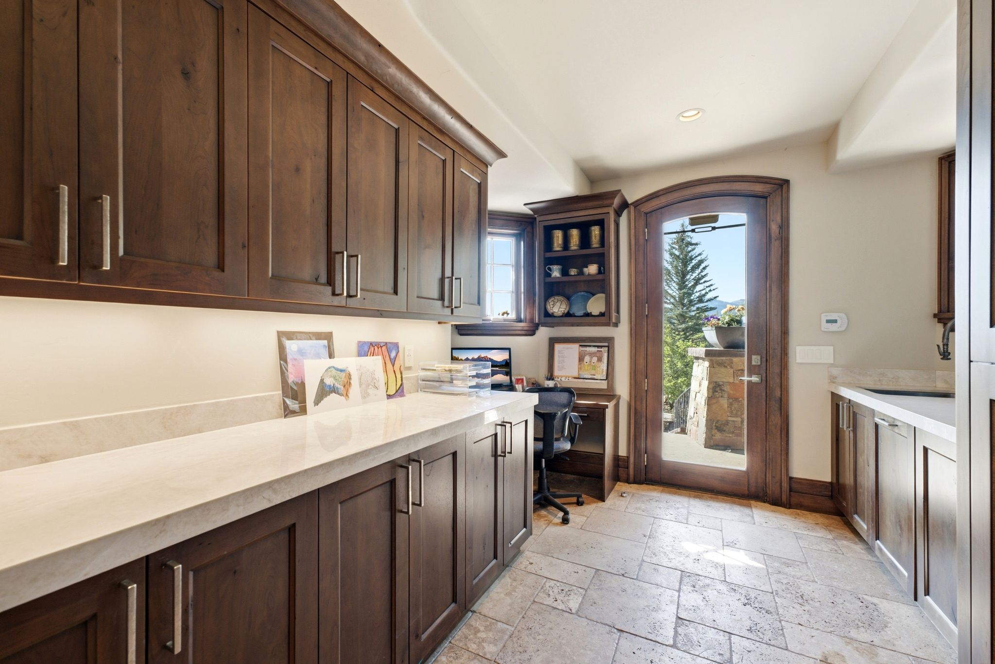 Custom cabinetry with integrated desk space, under-cabinet lighting, light-toned countertops, and stone tile flooring