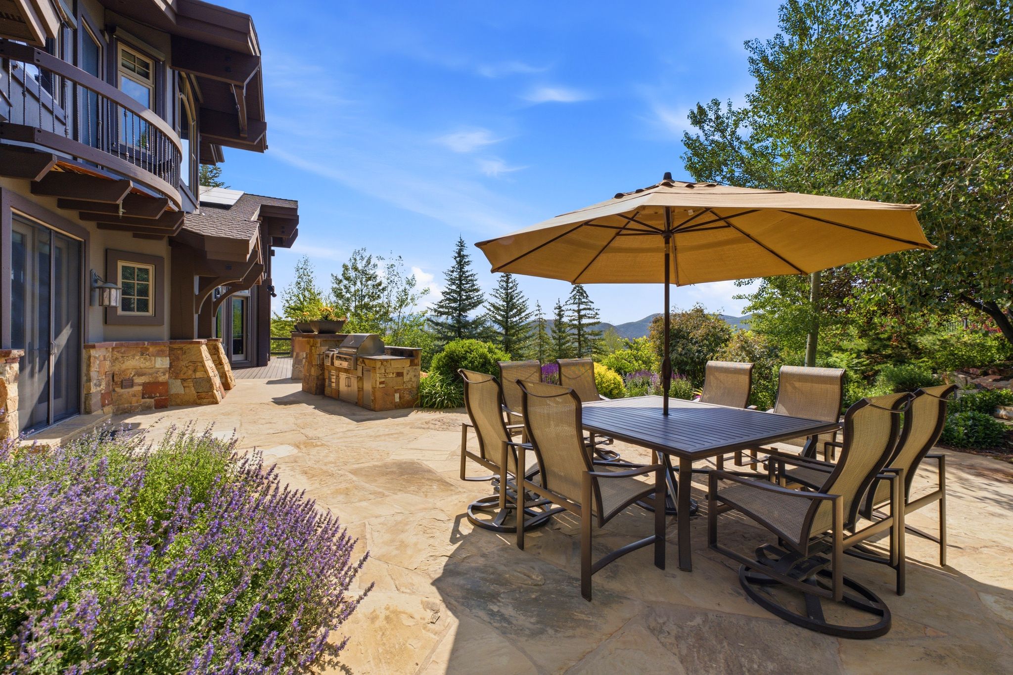 Spacious flagstone patio featuring a built-in outdoor kitchen with stone veneer, and mature landscaping