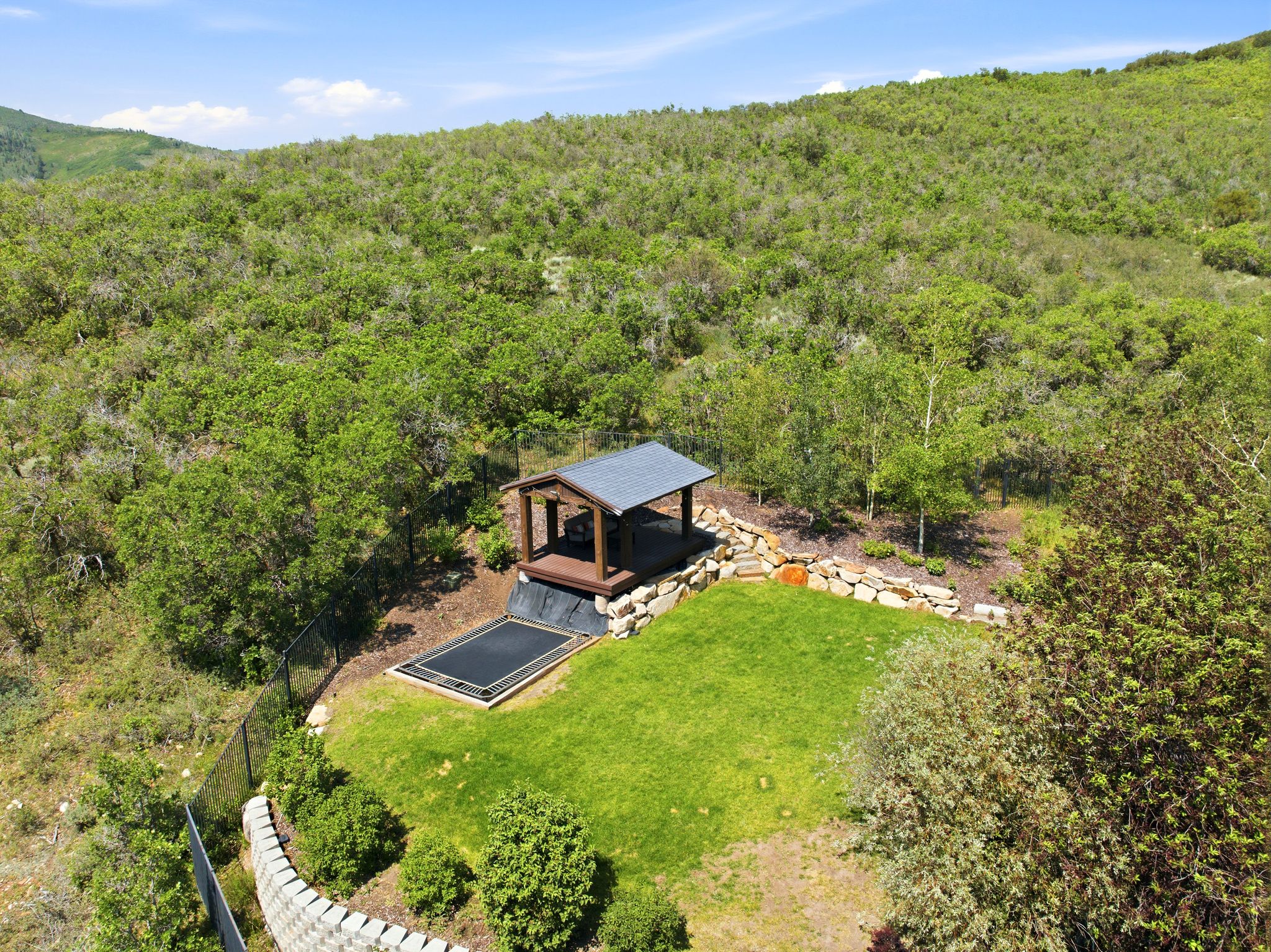 Sloped backyard featuring a covered gazebo structure, a level grassy area, and an in-ground trampoline